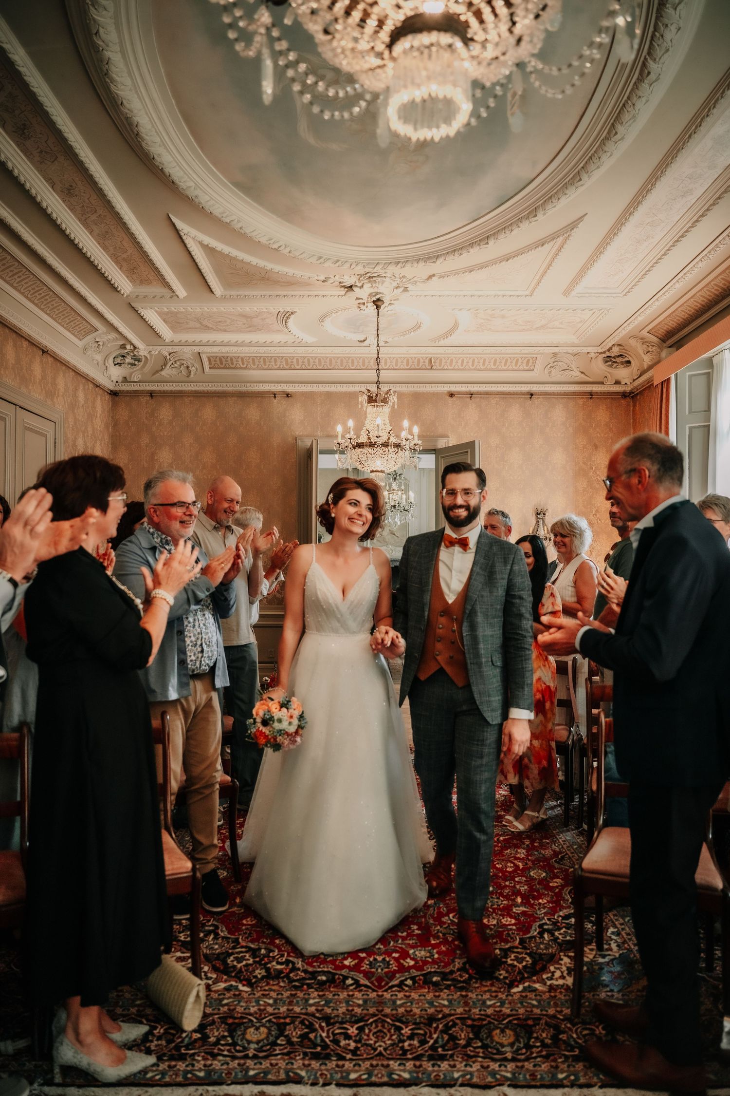 Six sequential photos show candid reception moments of a wedding party in an ornate ballroom with chandeliers and red carpet.