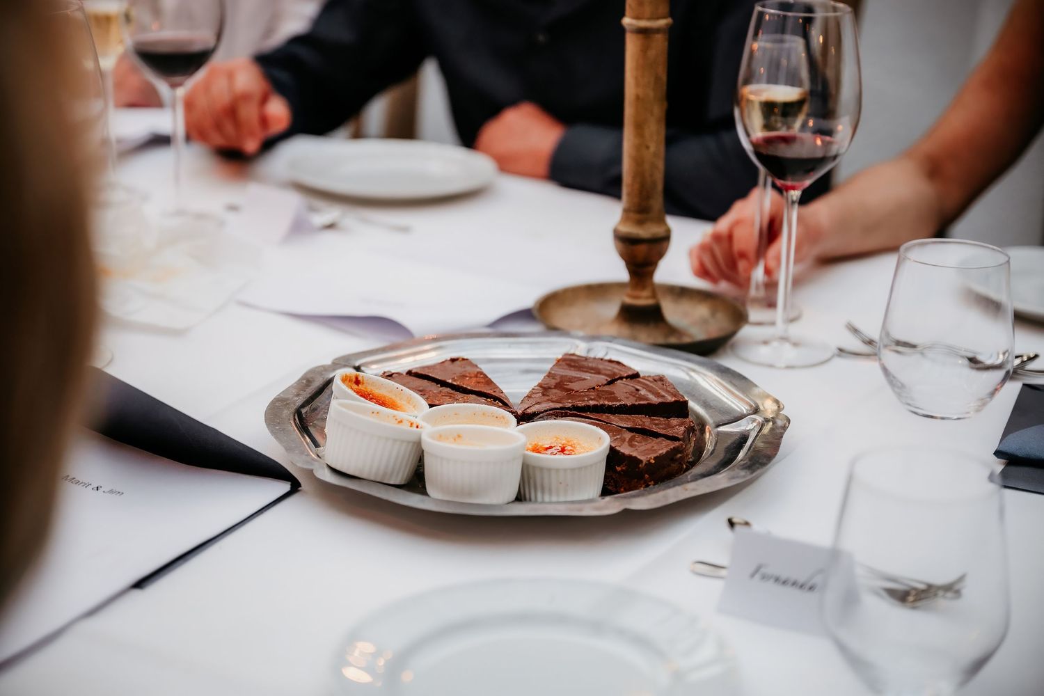 Close-up of charcuterie plate with wine glasses on elegant white tablecloth.