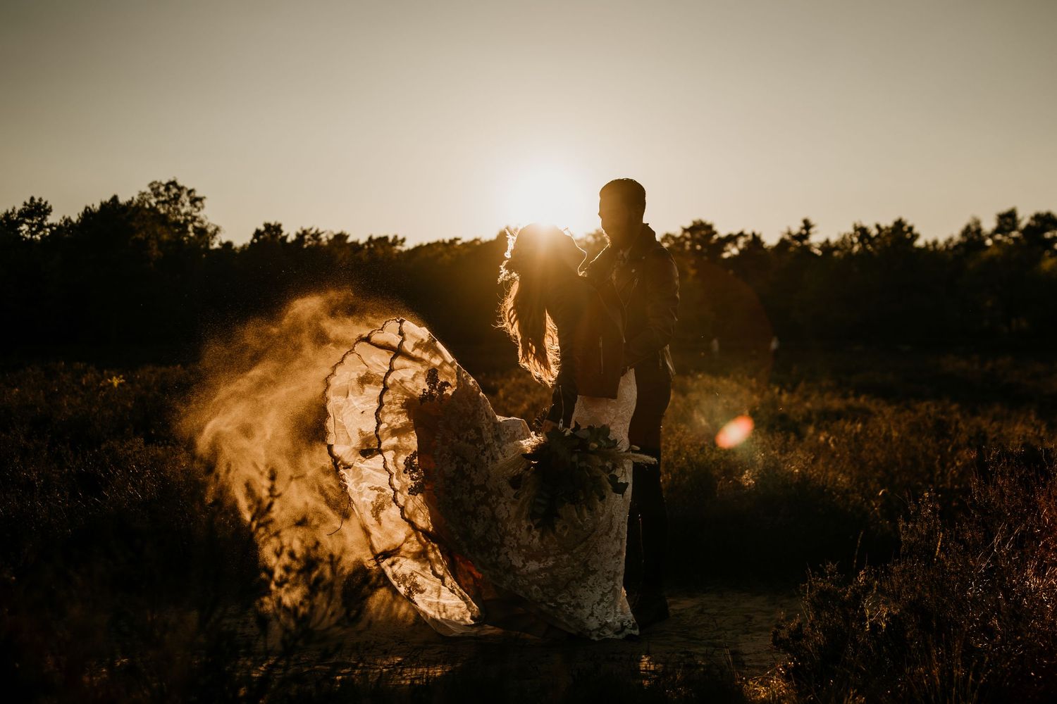 Golden sunset silhouettes at an outdoor wedding celebration.