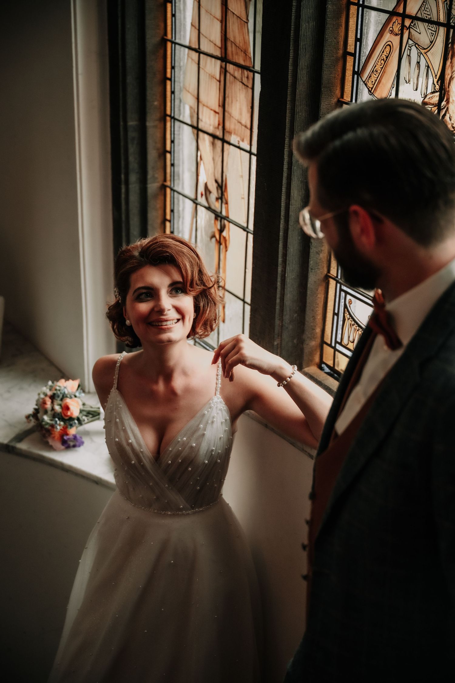 Intimate moment captured by window light showing wedding dress details and natural expressions.