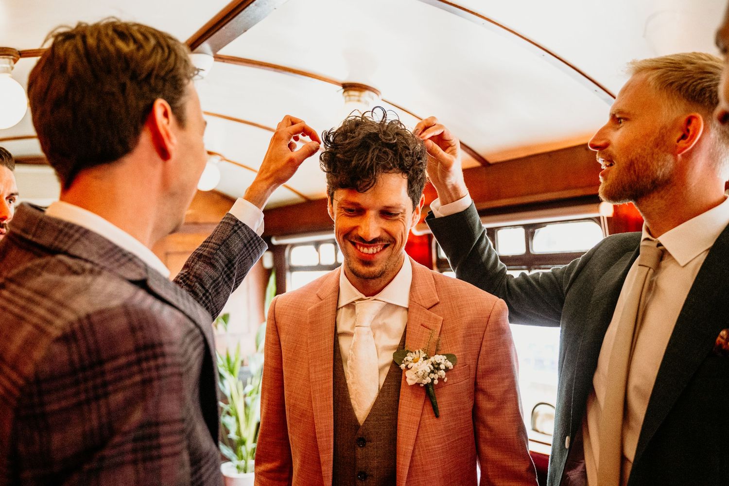 Groomsmen in brown suits and plaid shirts share candid laughs during a wedding celebration.