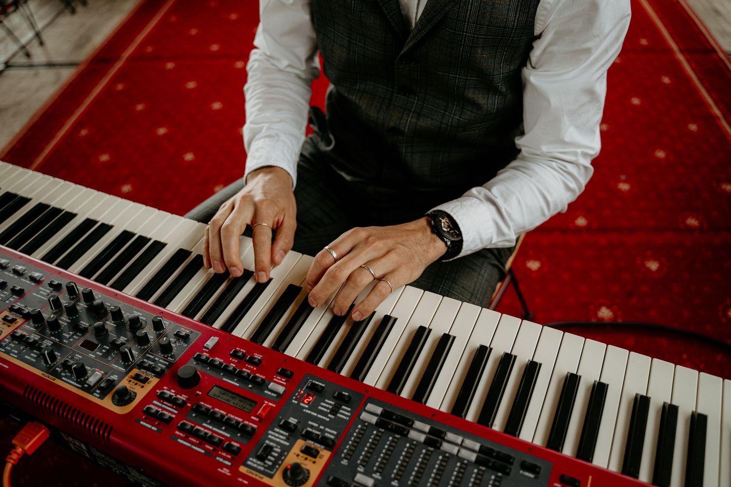 Hands playing piano keys on red velvet stage.