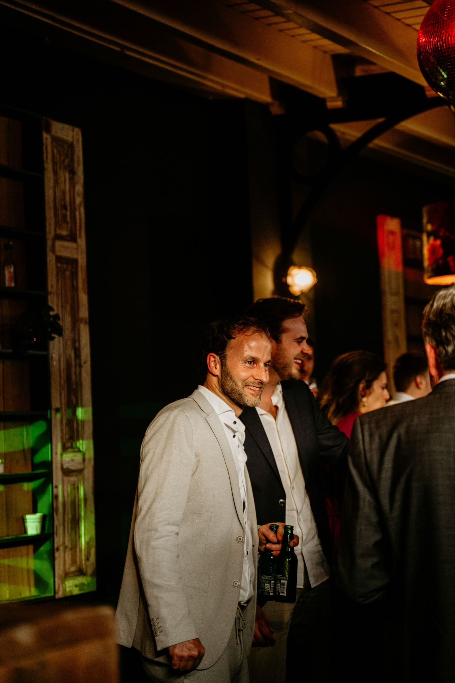 People in formal attire gather in a dimly lit venue with dramatic lighting and dark ambiance.