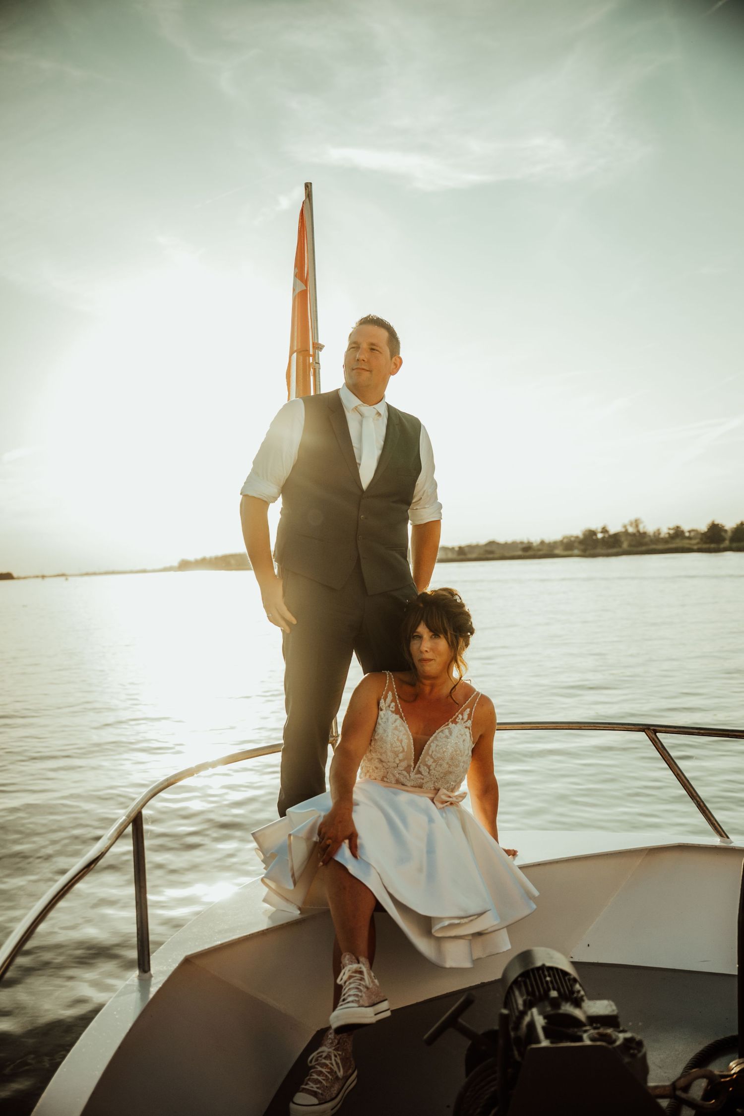 A couple stands together on a boat during sunset over a calm lake while enjoying a romantic moment.