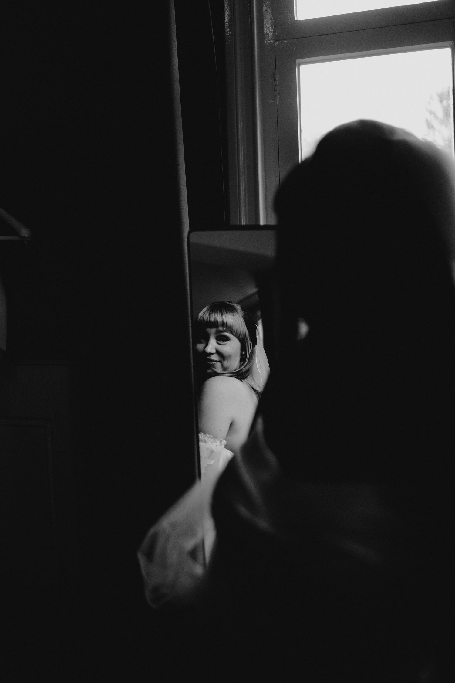 Dramatic black and white portrait showing a silhouetted figure near a window with natural light.
