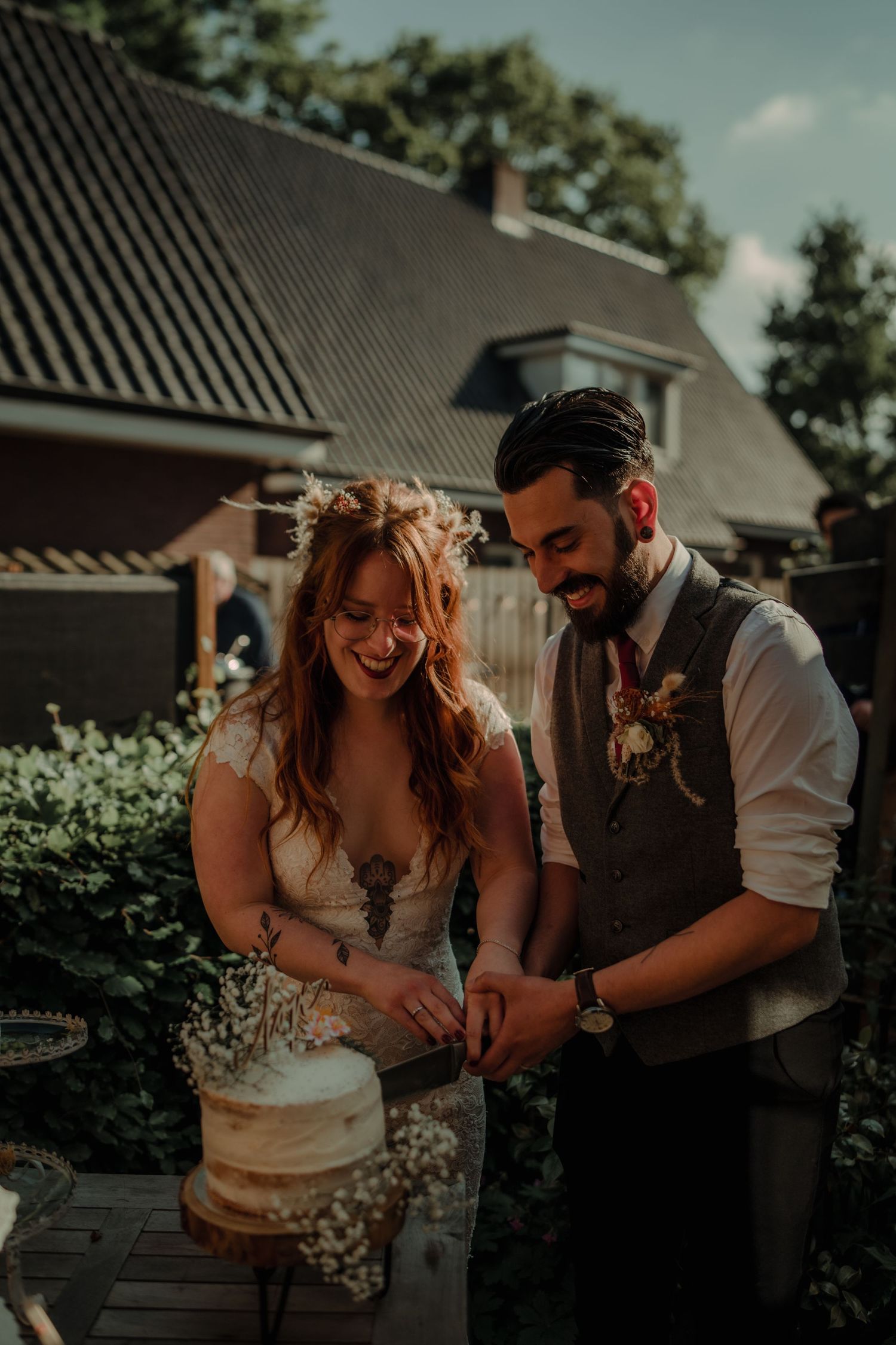 A couple shares a joyful moment while cutting their wedding cake in a garden setting.