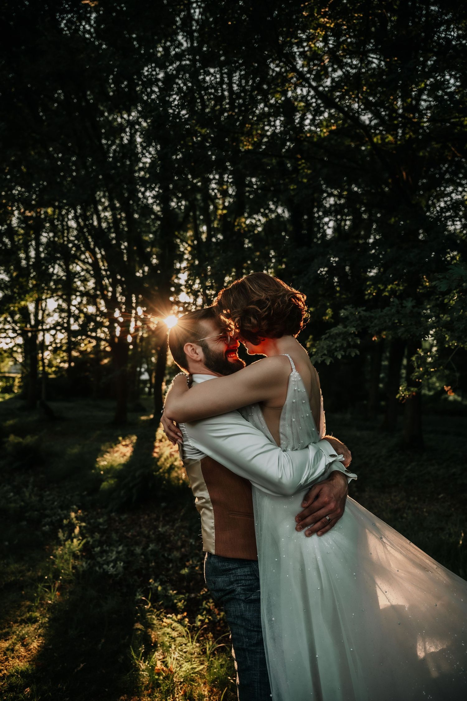 Newlyweds embrace in a golden sunset forest setting for romantic wedding portraits.