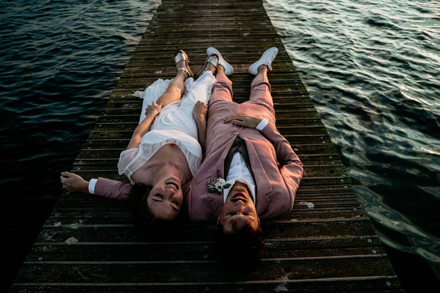 Couple lying on wooden dock over water at sunset.