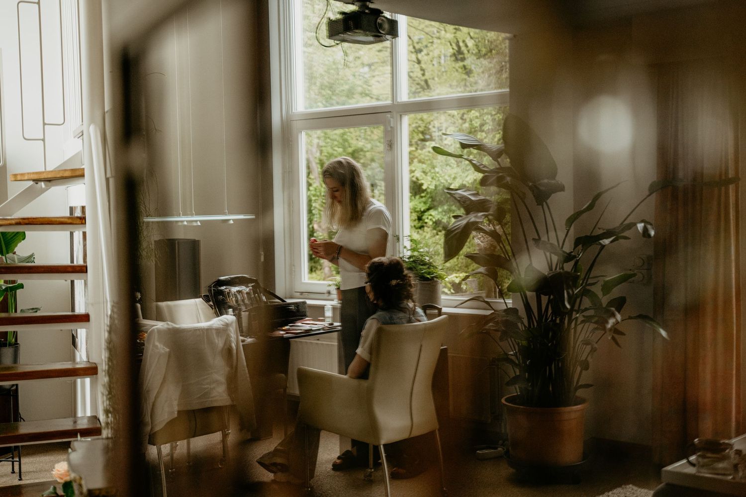 Elegant bridal preparation scene in a sunlit room with white decor and wooden shelving.