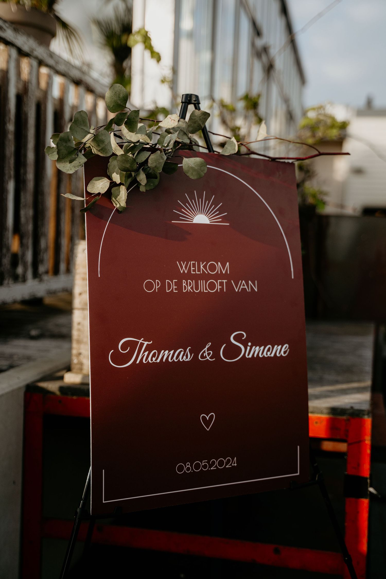 Burgundy wedding welcome sign with elegant white lettering and greenery decoration.
