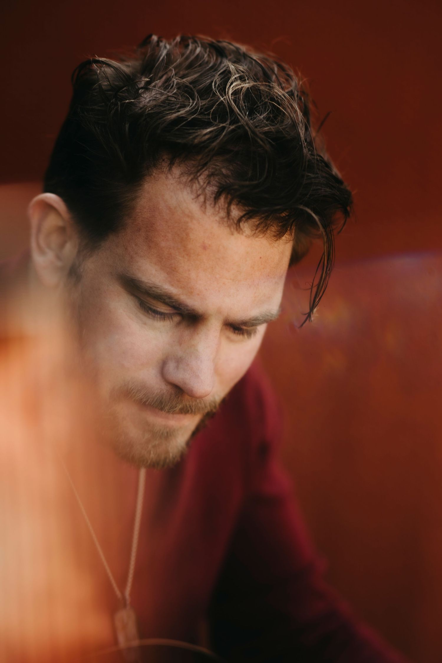 A person's profile view in low light against a dark red background, showing contemplative expression.