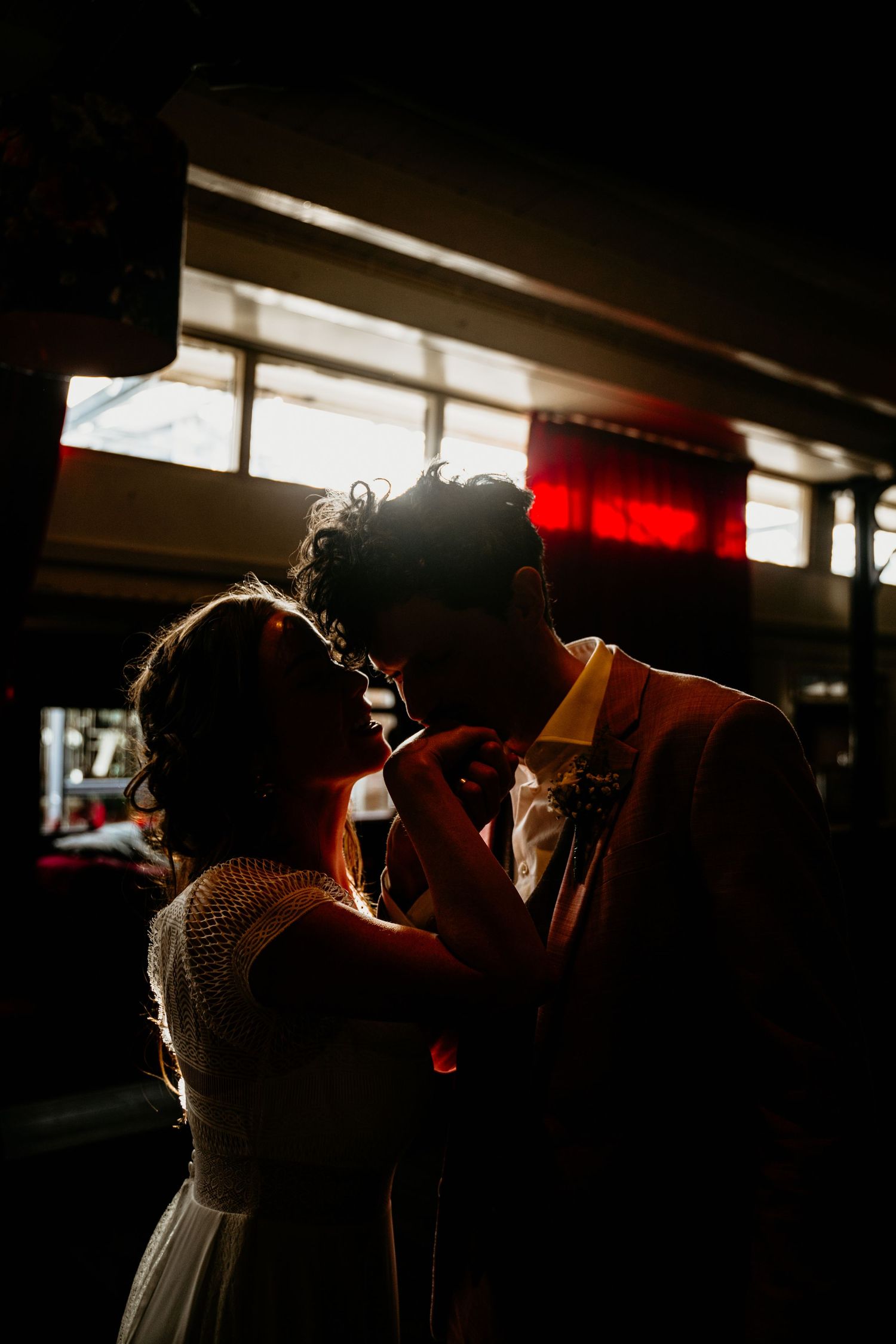 Dramatic backlit silhouettes of wedding couple in an indoor venue with streaming light.