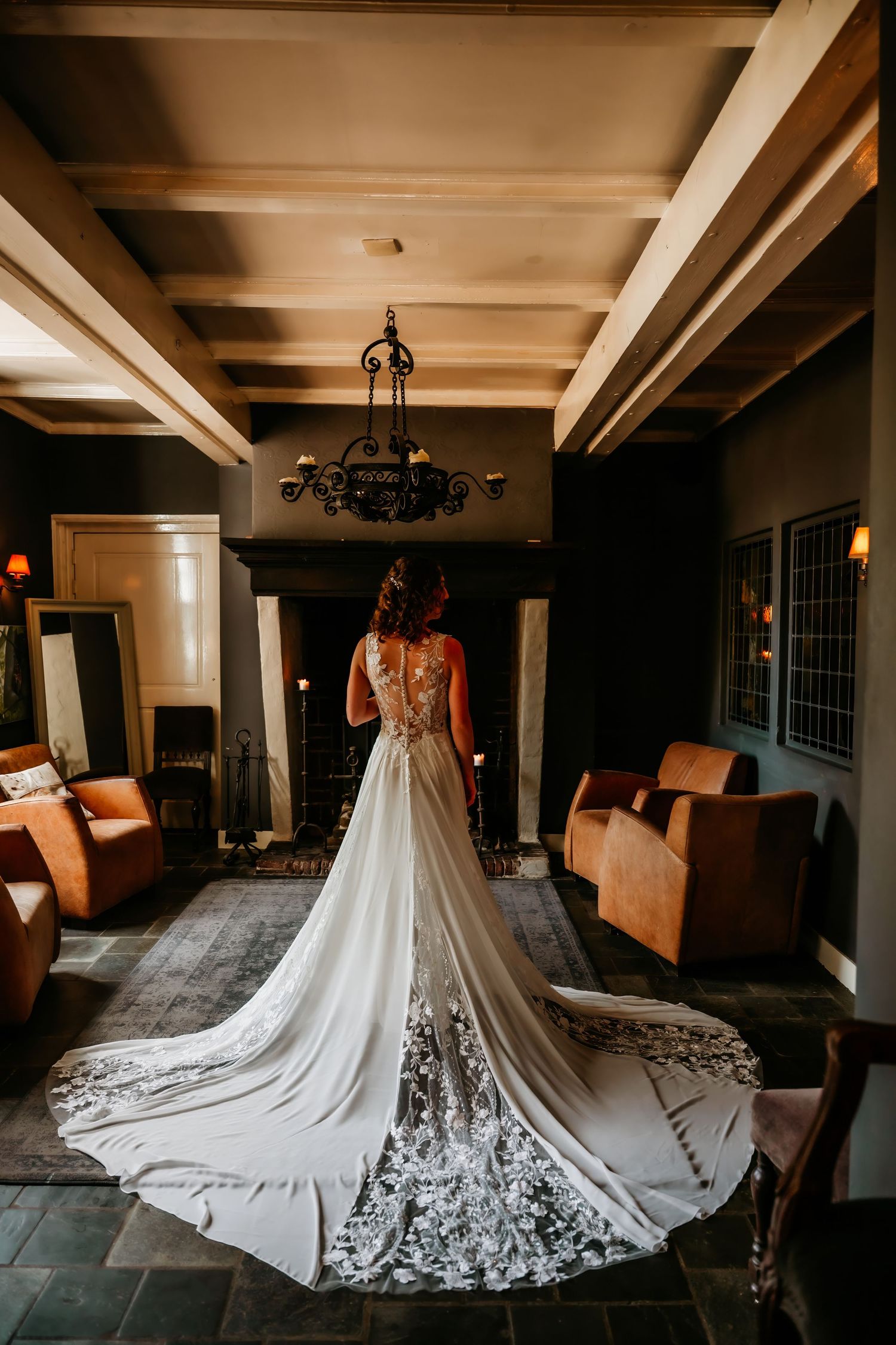A stunning wedding dress with intricate lace details and flowing train photographed from behind in an elegant room.