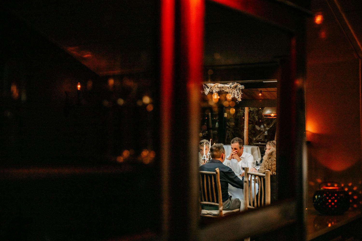 Through a window, guests can be seen dining at tables in a warmly lit evening reception.