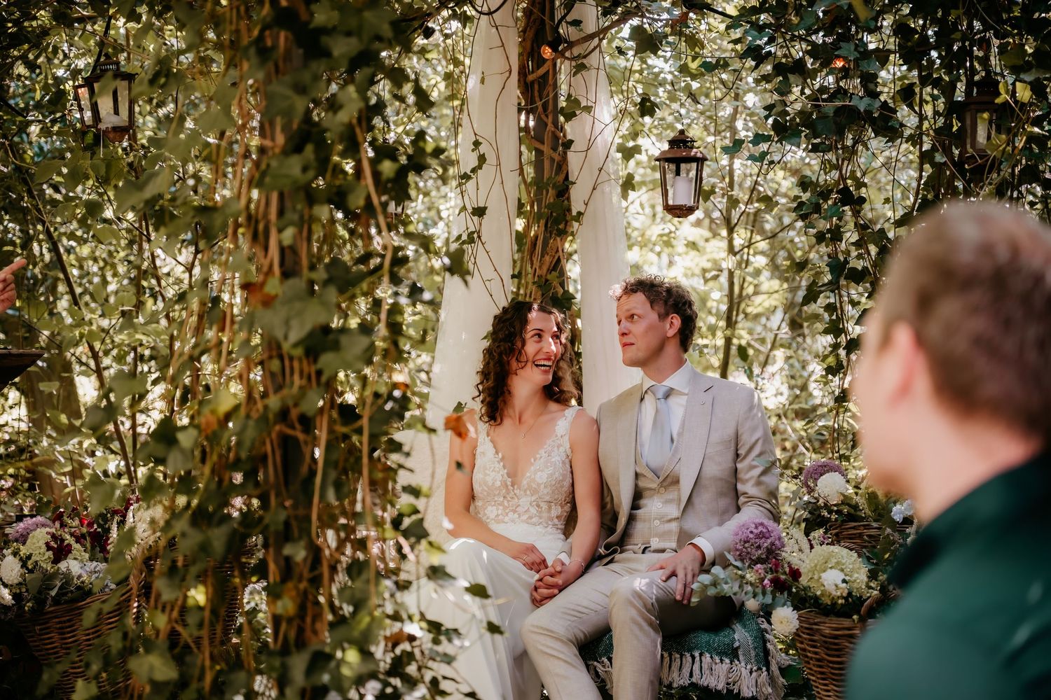 A couple shares an intimate moment while seated under a canopy of green leaves.