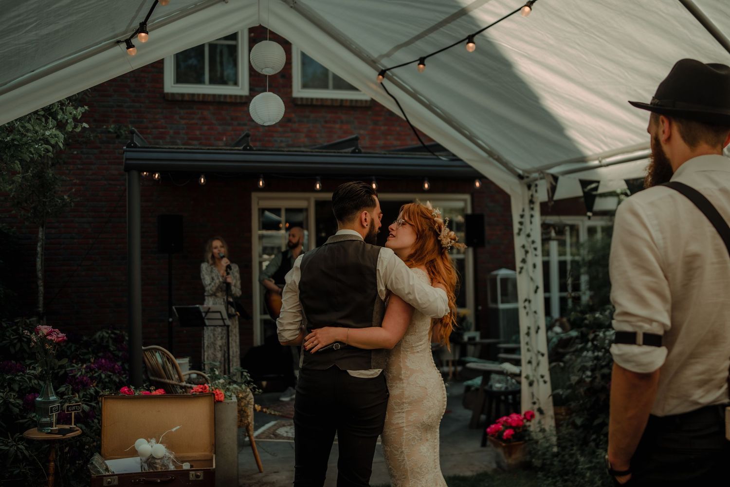 A wedding reception under a white tent with string lights and floral arrangements.