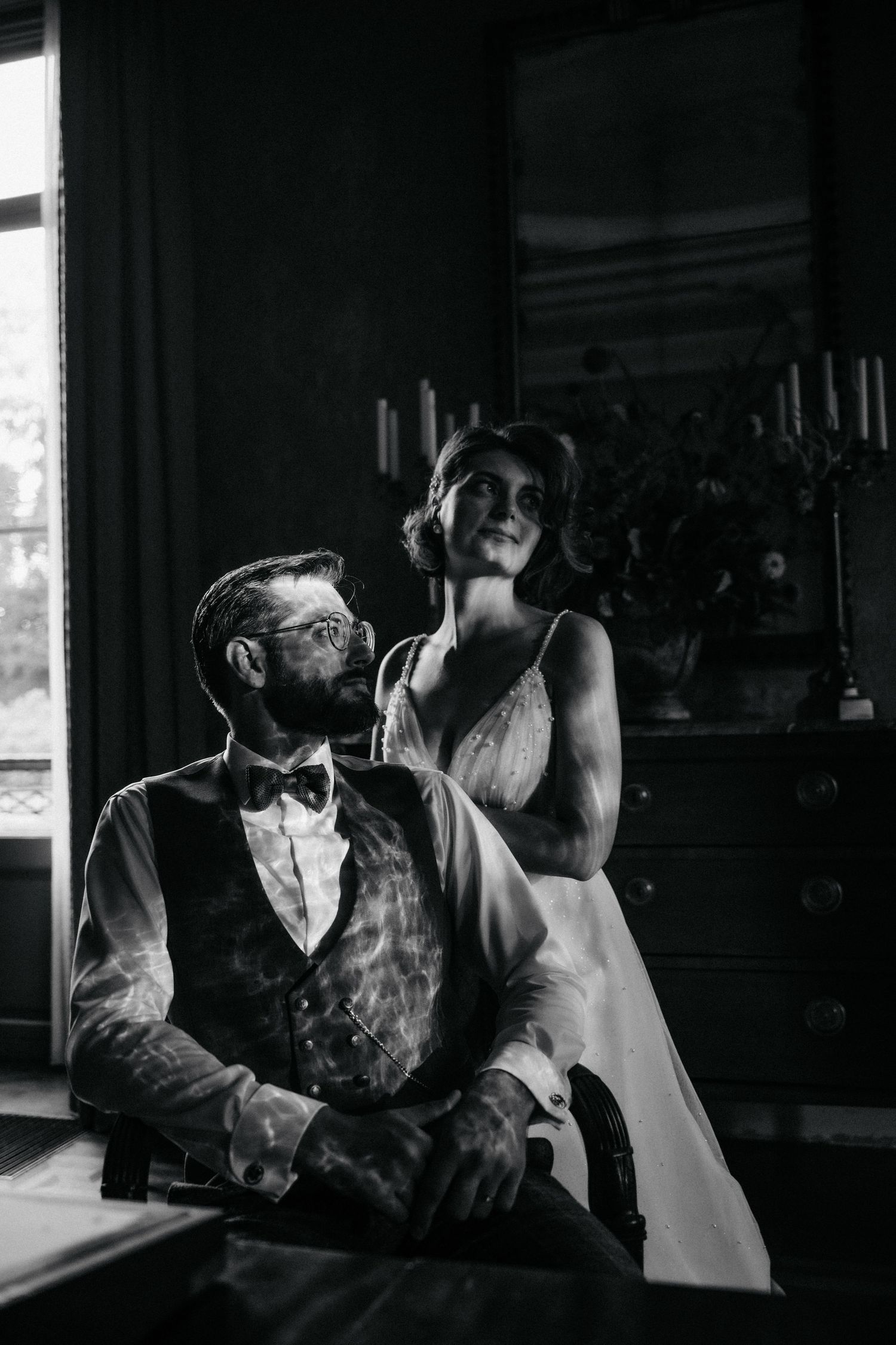 A romantic black and white wedding photo near a window with vintage decor.
