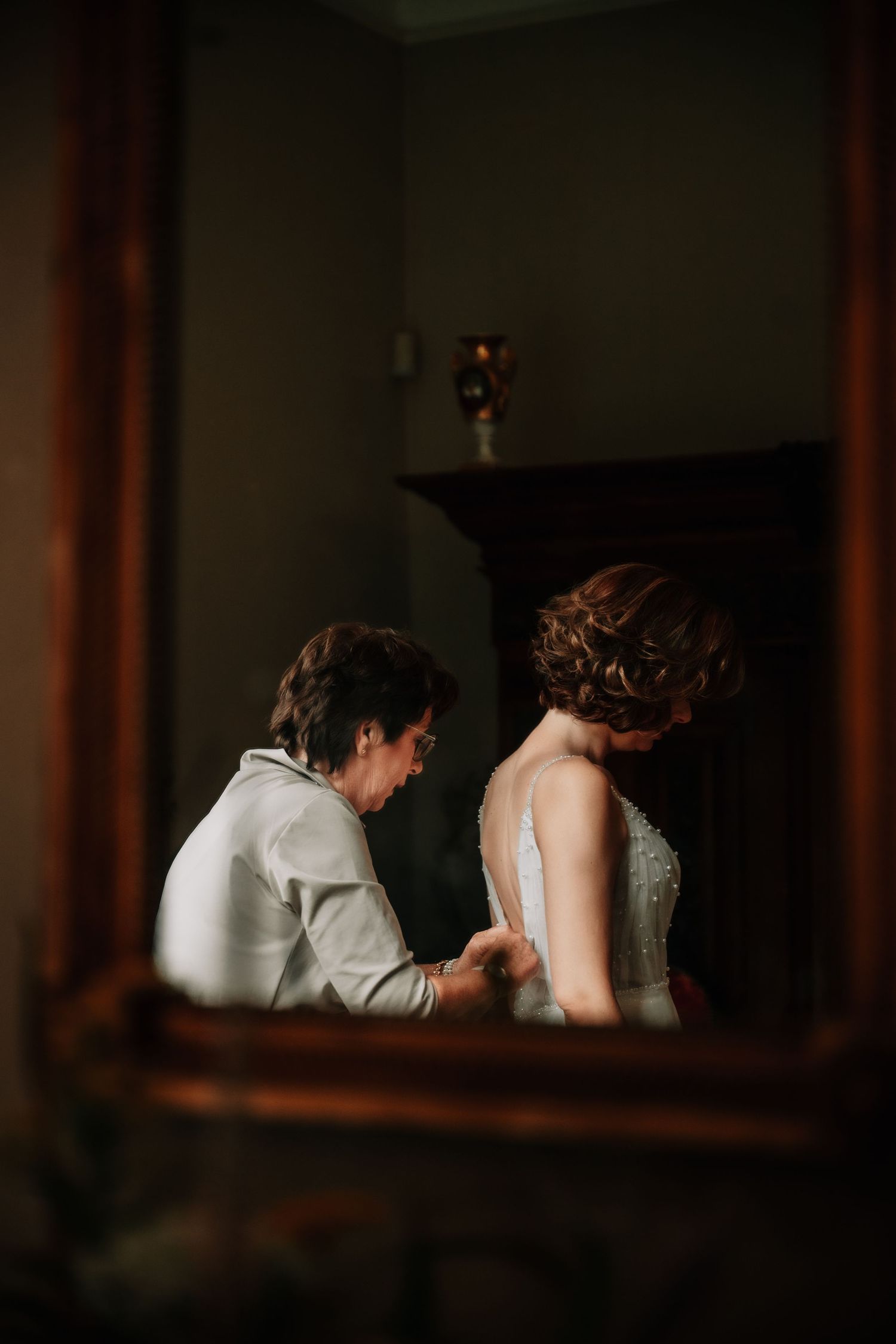 Intimate moment captured through a window frame in dark, moody lighting.