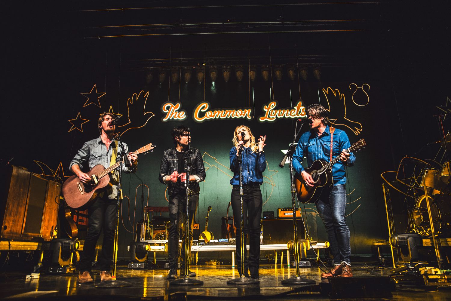 Musicians perform on stage at The Commons Live with acoustic guitars and microphones under warm lighting.