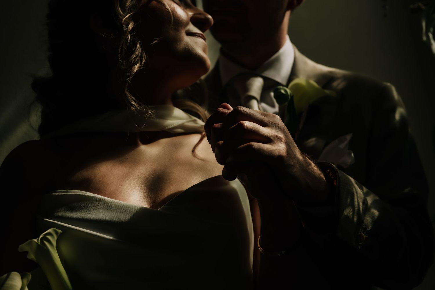A bride and groom share an intimate moment, her hand resting on his chest in dramatic moody lighting.