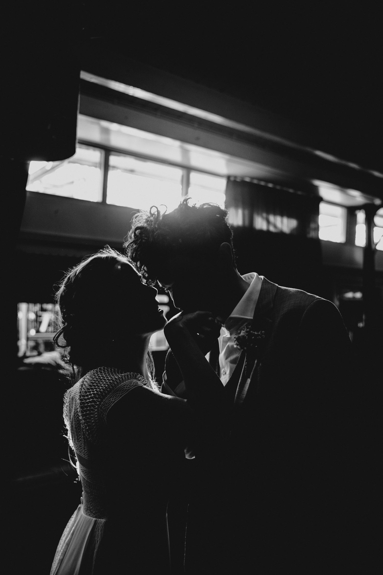 Silhouettes of wedding couple embracing in dramatic indoor lighting.