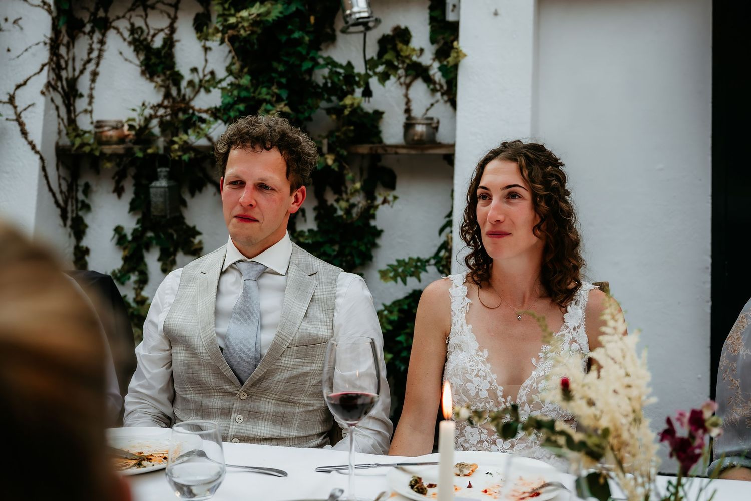 Wedding couple seated at reception table with white floral centerpieces.