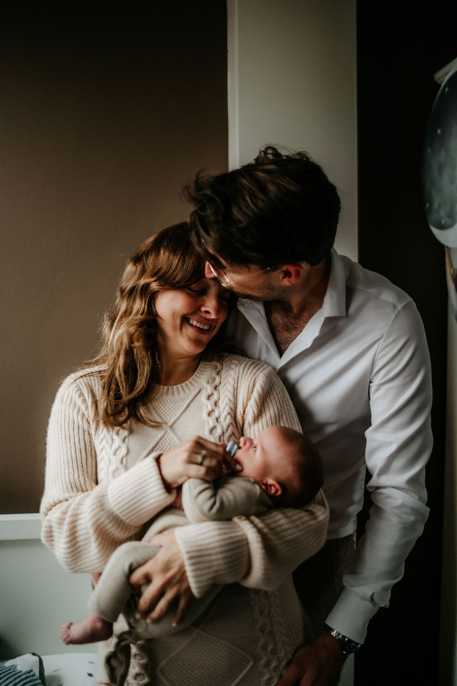 Tender moment between couple with newborn baby against window light.