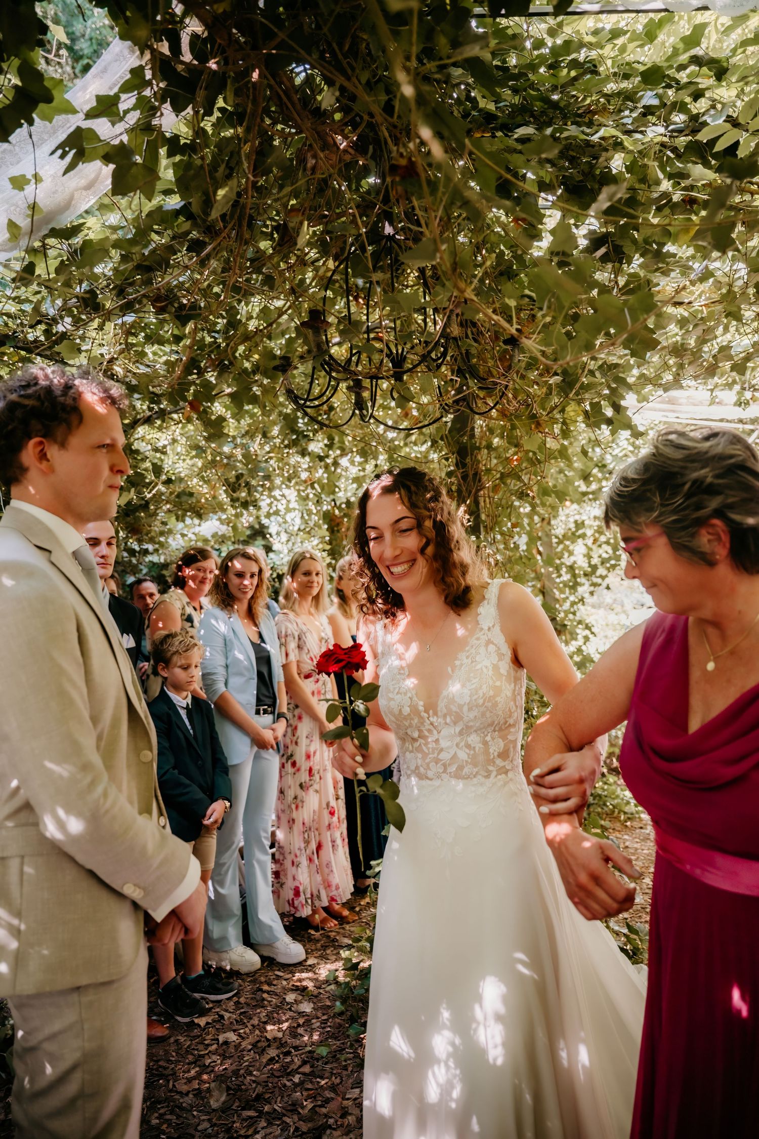 A joyful wedding celebration under a leafy canopy with guests in summer attire and floral dresses.
