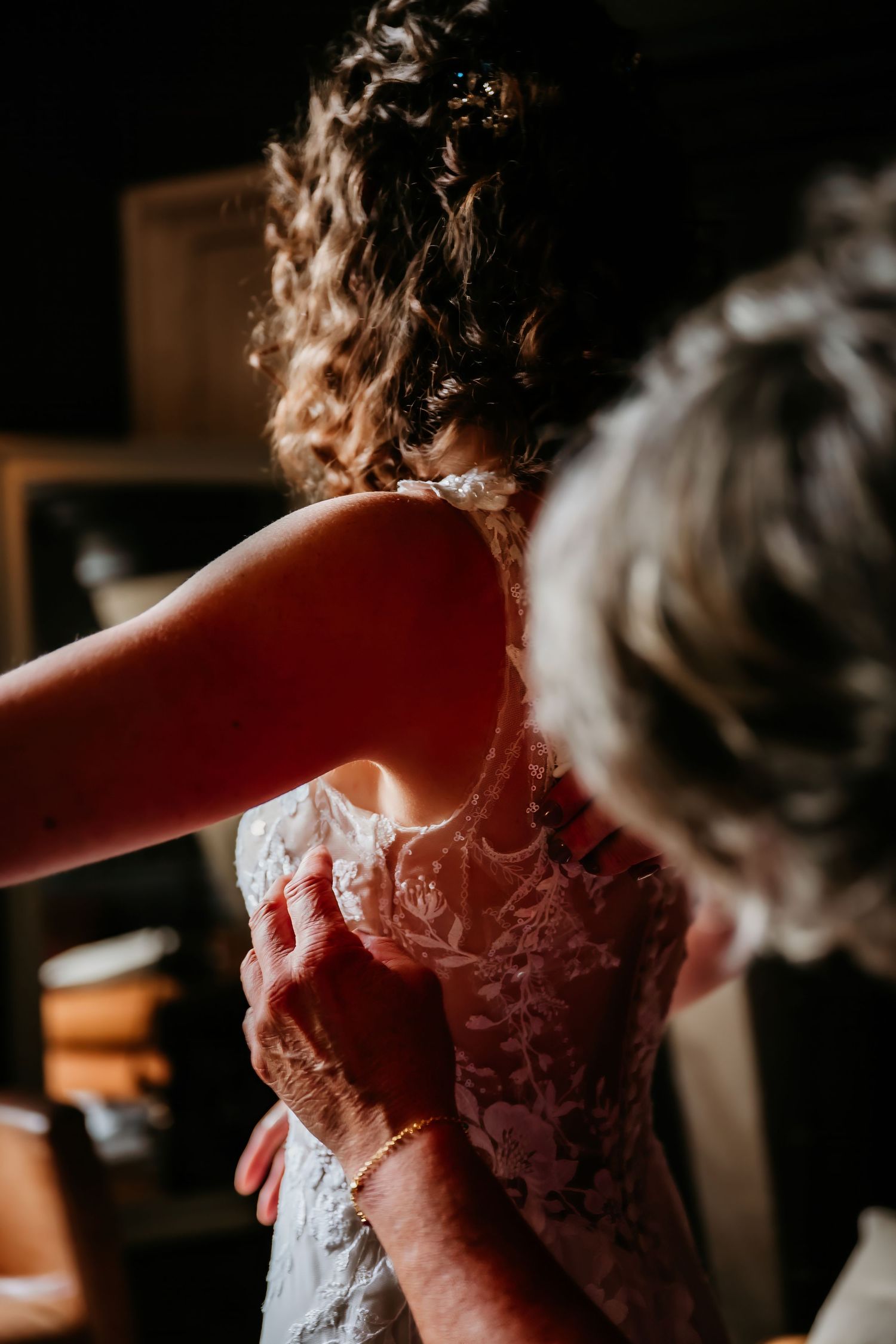 Close-up details of a delicate lace wedding dress being fastened in natural lighting.