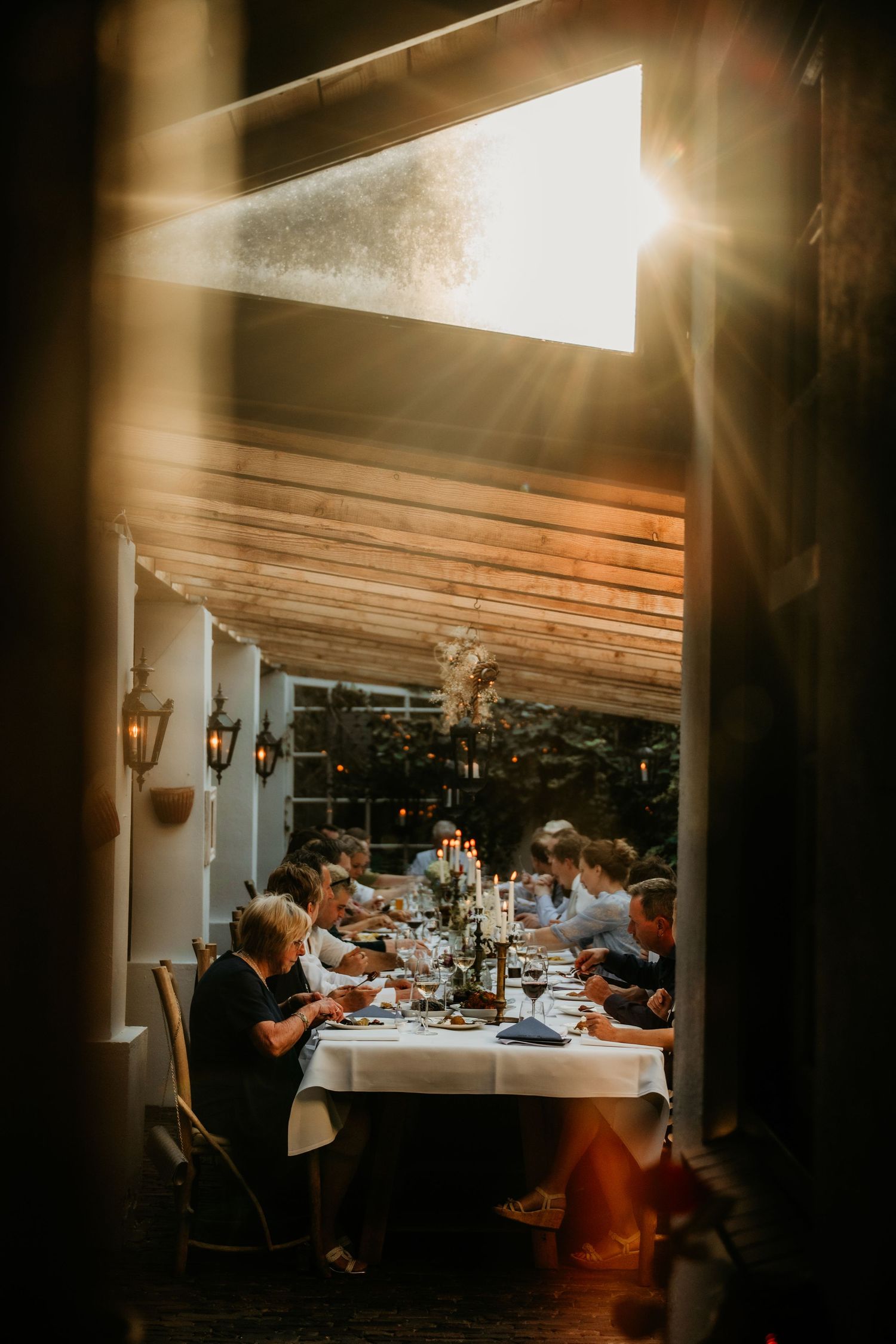 Wedding reception dinner scene captured through a doorway with warm lighting and guests seated at a long table.