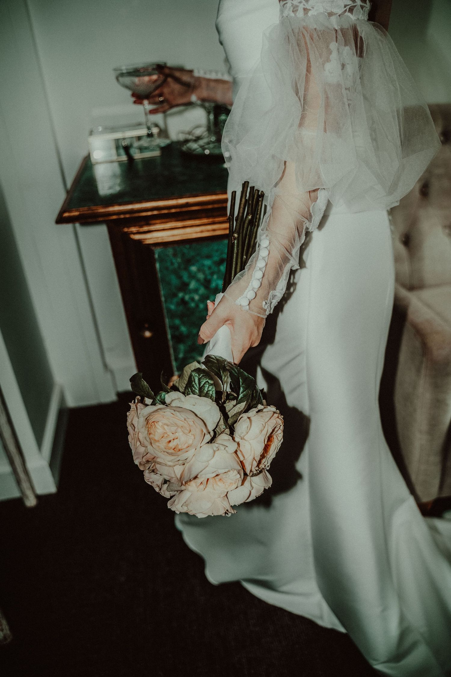 A close-up of a bride's elegant white dress and peach-colored wedding bouquet against a dark background.