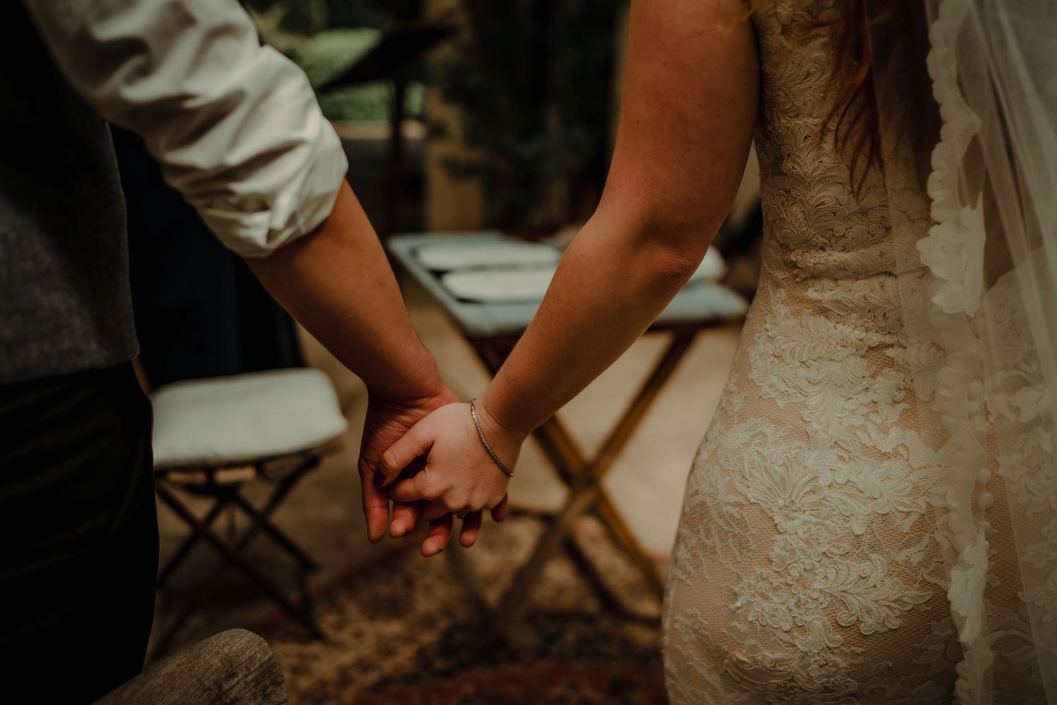 Close-up of couple holding hands showing lace wedding dress detail.