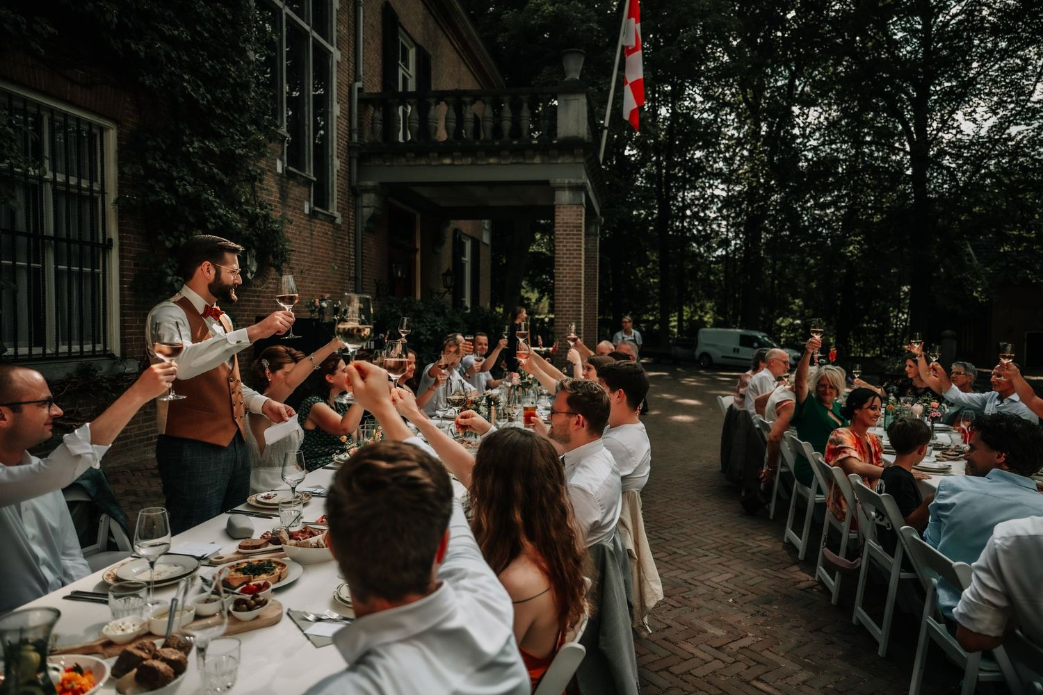 Wedding guests raise their glasses in celebration during an outdoor reception dinner.