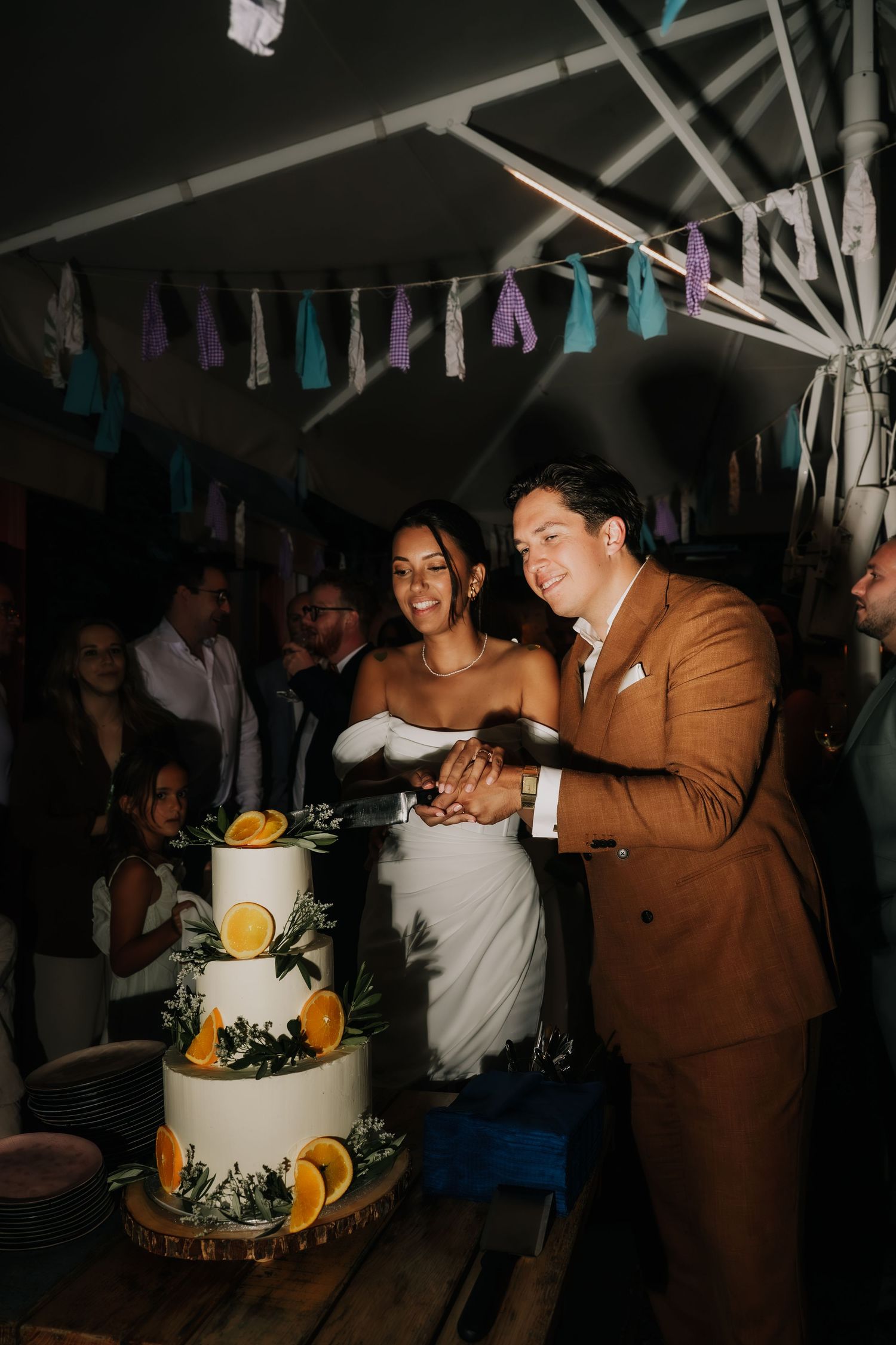 Bride and groom cutting a white wedding cake decorated with orange slices at their outdoor reception.