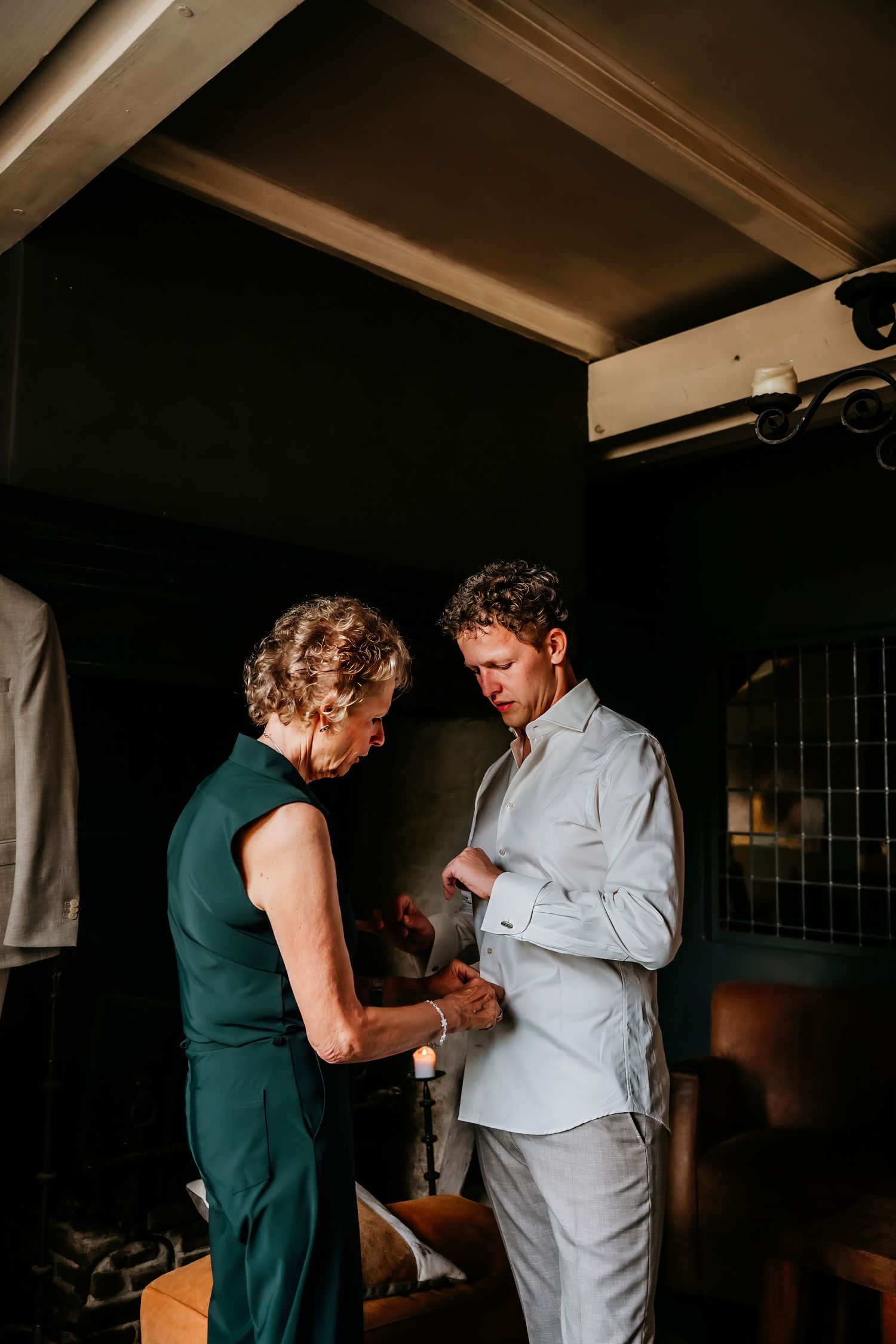Getting ready for a wedding ceremony as a light grey suit is being adjusted in a dimly lit room.