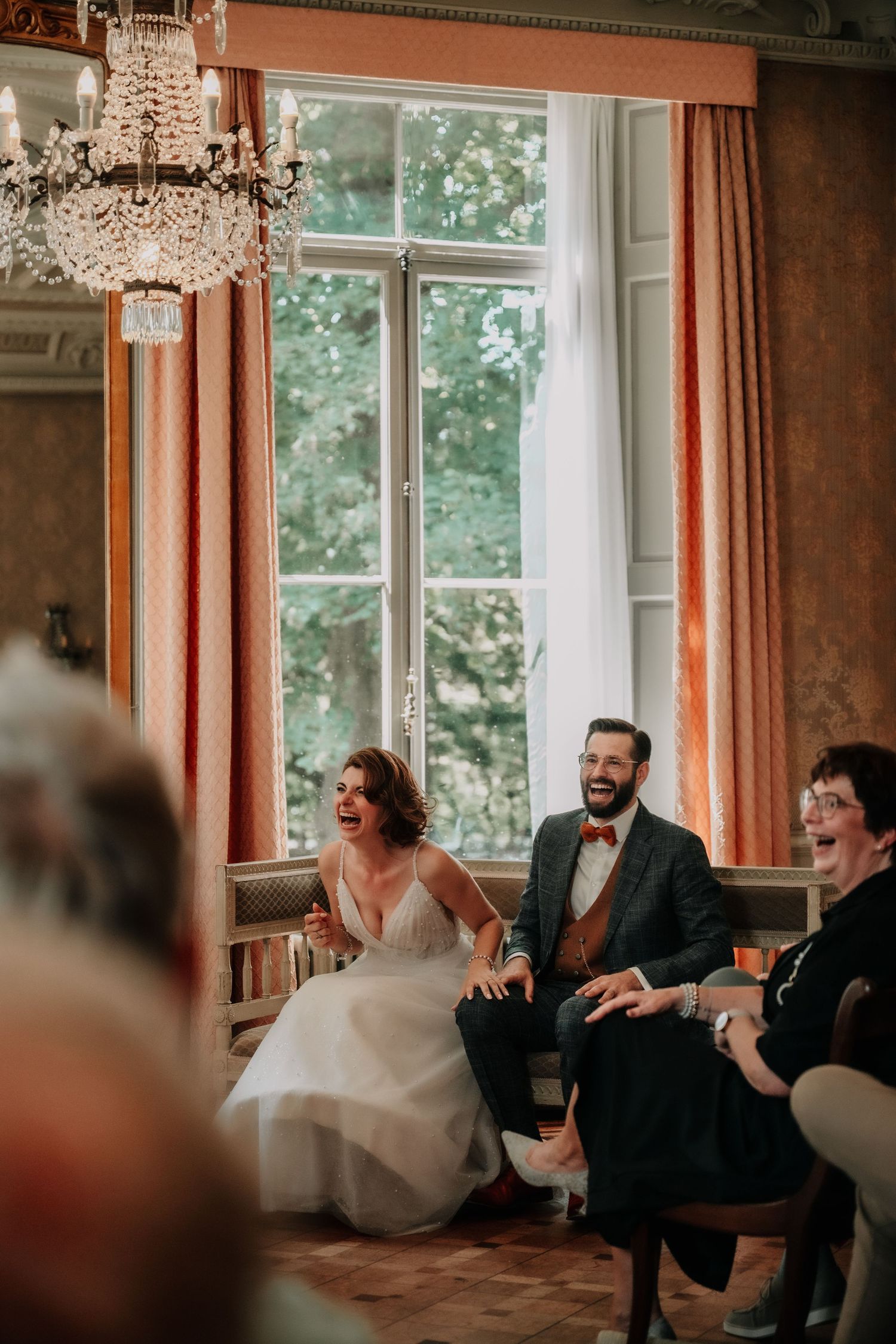 A joyful moment shared in an elegant room with crystal chandeliers and orange curtains.