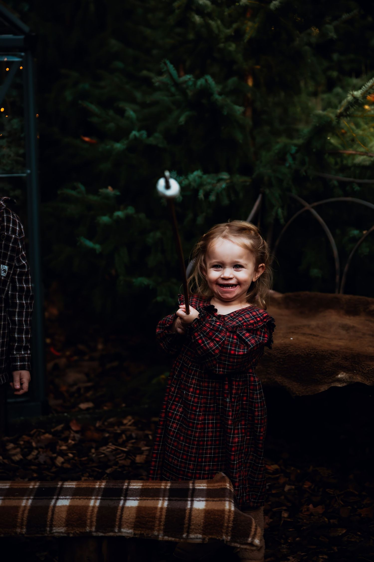A child in a red plaid dress sits on a blanket outdoors during an autumn photoshoot.