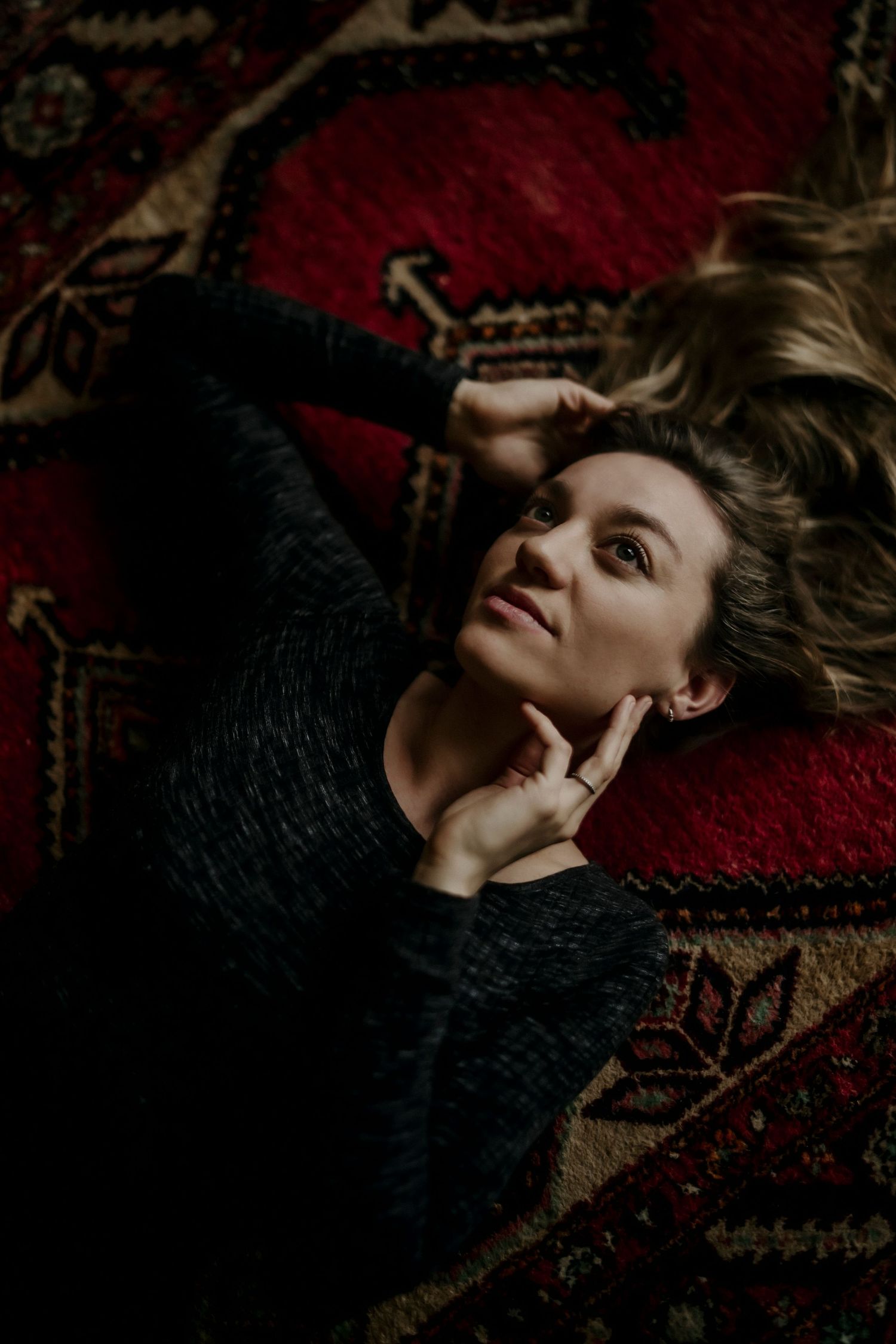 A person lies on a dark textured surface with dramatic shadows and moody lighting creating an artistic portrait.