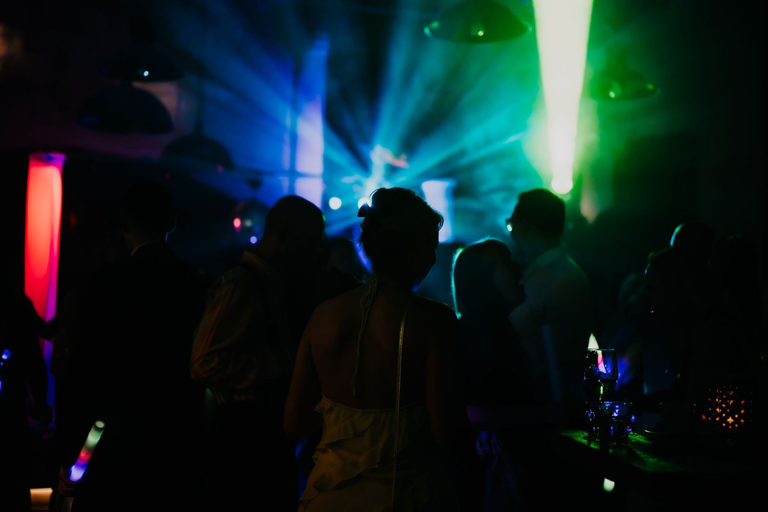Silhouettes of people dancing in a nightclub with colorful laser lights in green, blue, and red.