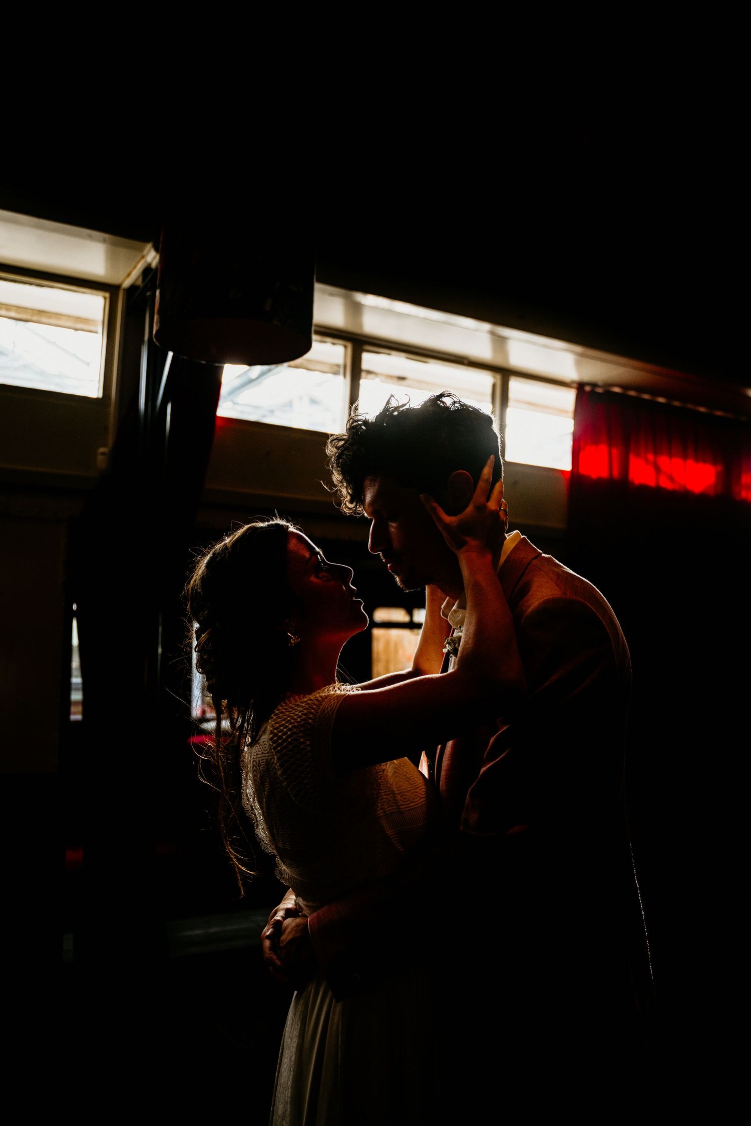 Silhouetted wedding couple sharing intimate moments in dramatic window lighting.