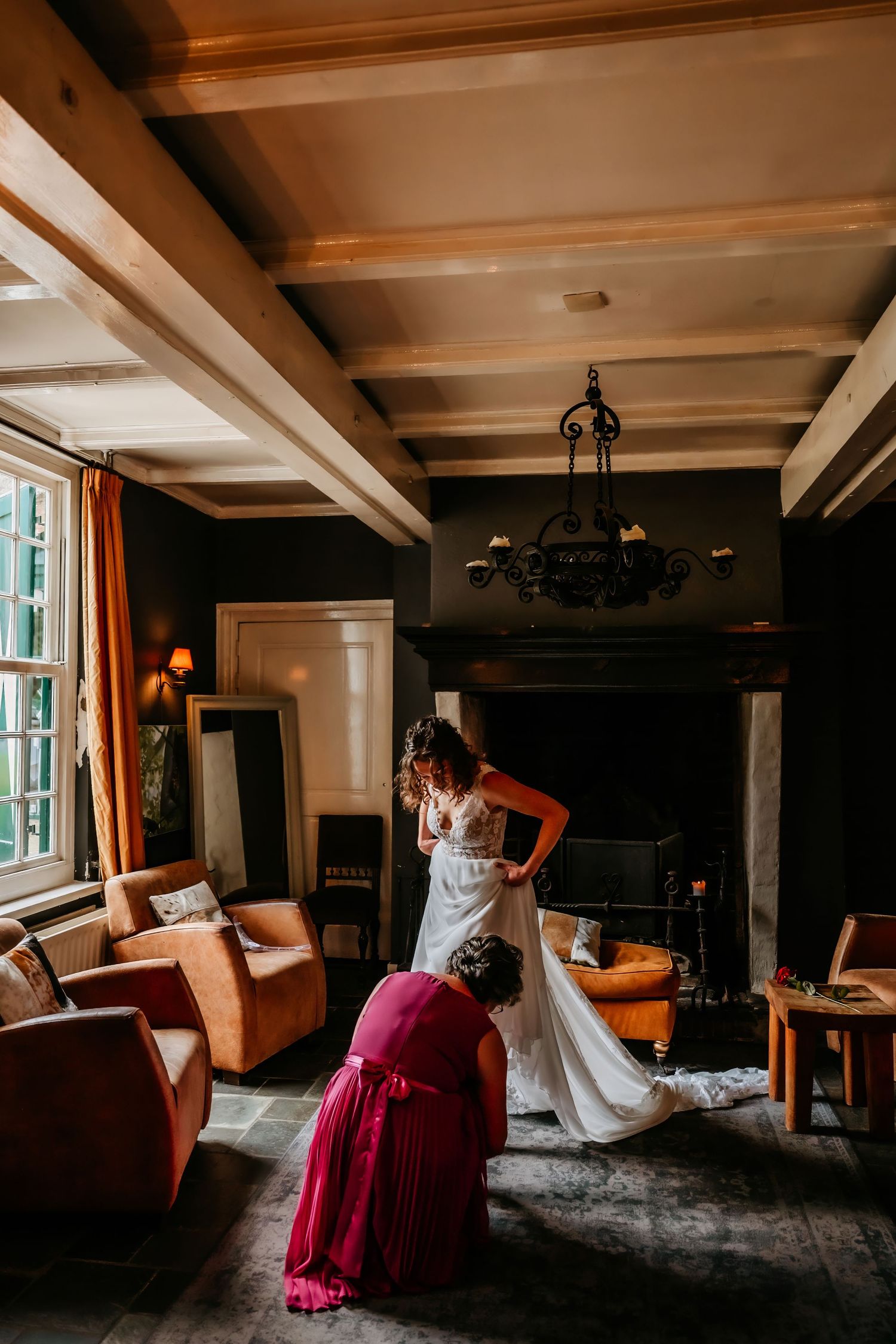 Wedding dress being adjusted in rustic room with wooden beams and vintage furniture.