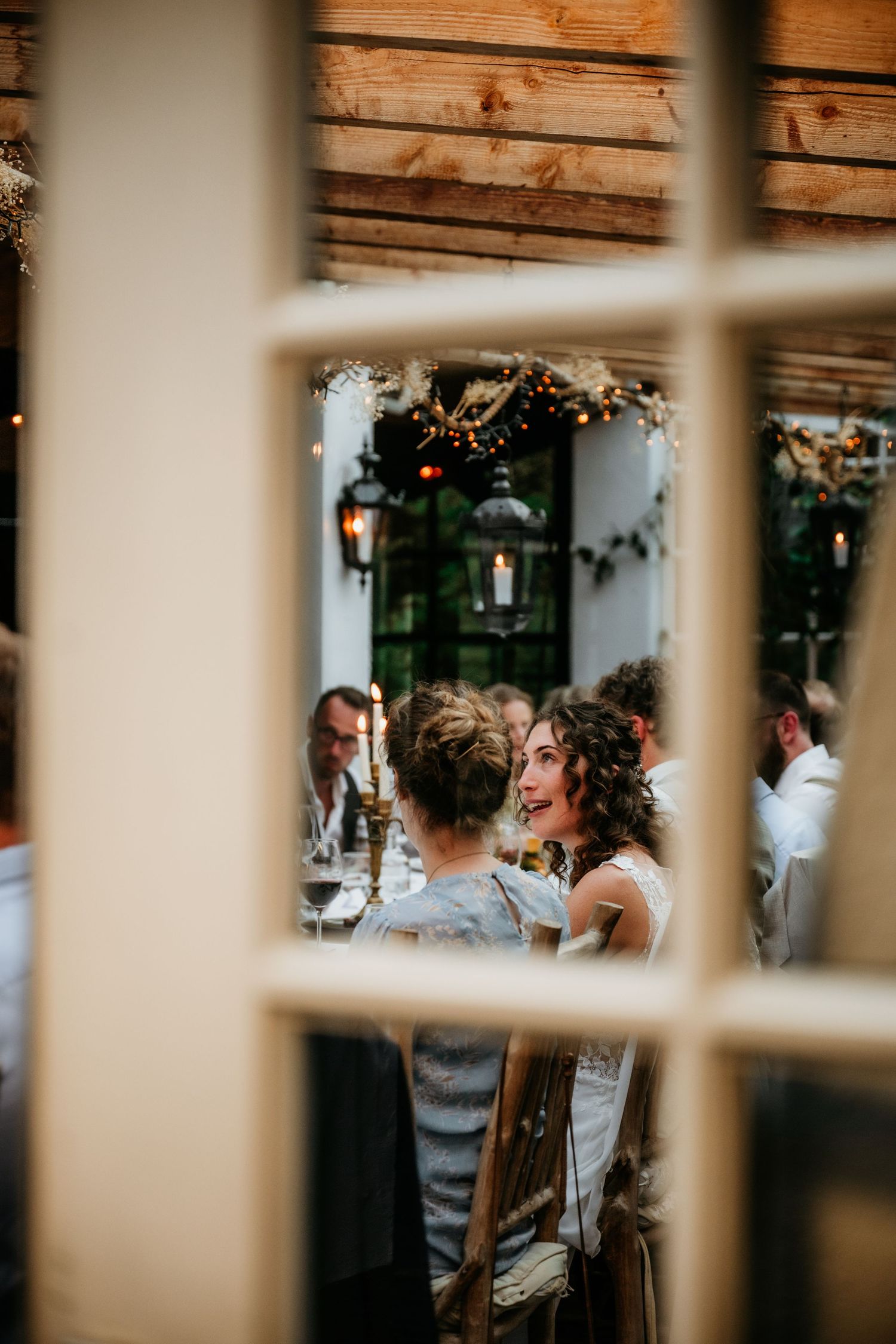 Wedding reception scene viewed through window panes with wooden beams overhead.