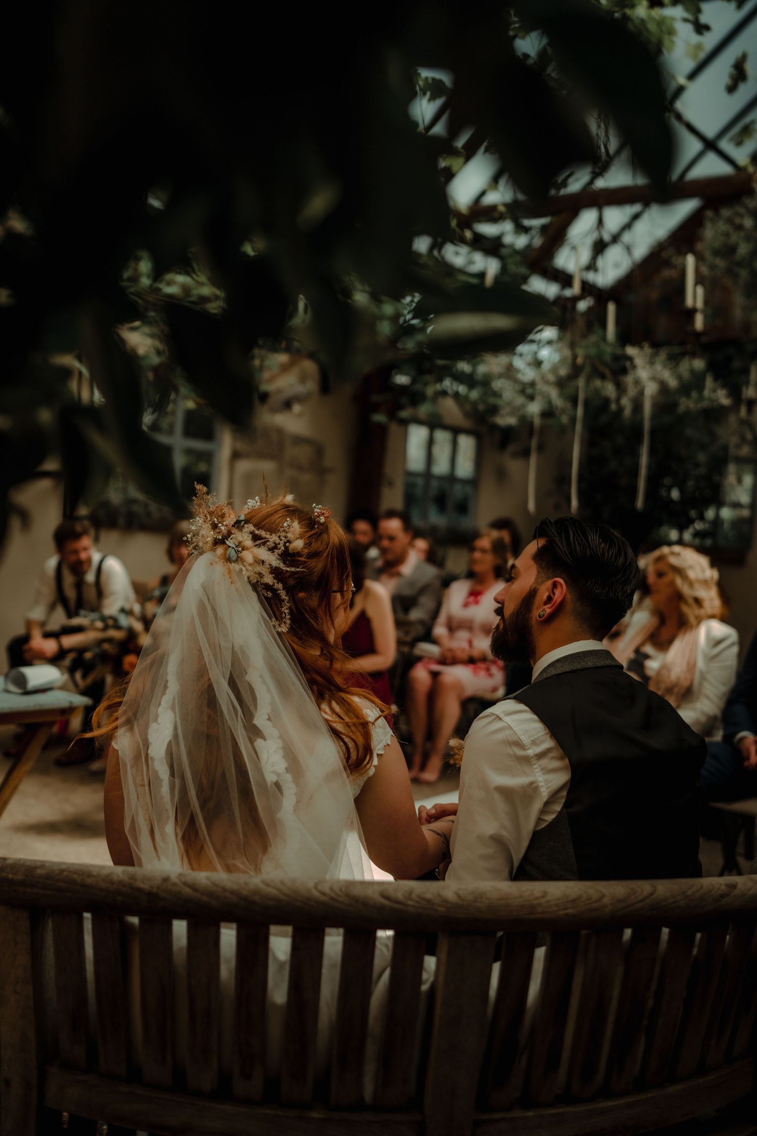 Wedding couple seated at rustic outdoor venue with floral crown and veil details.
