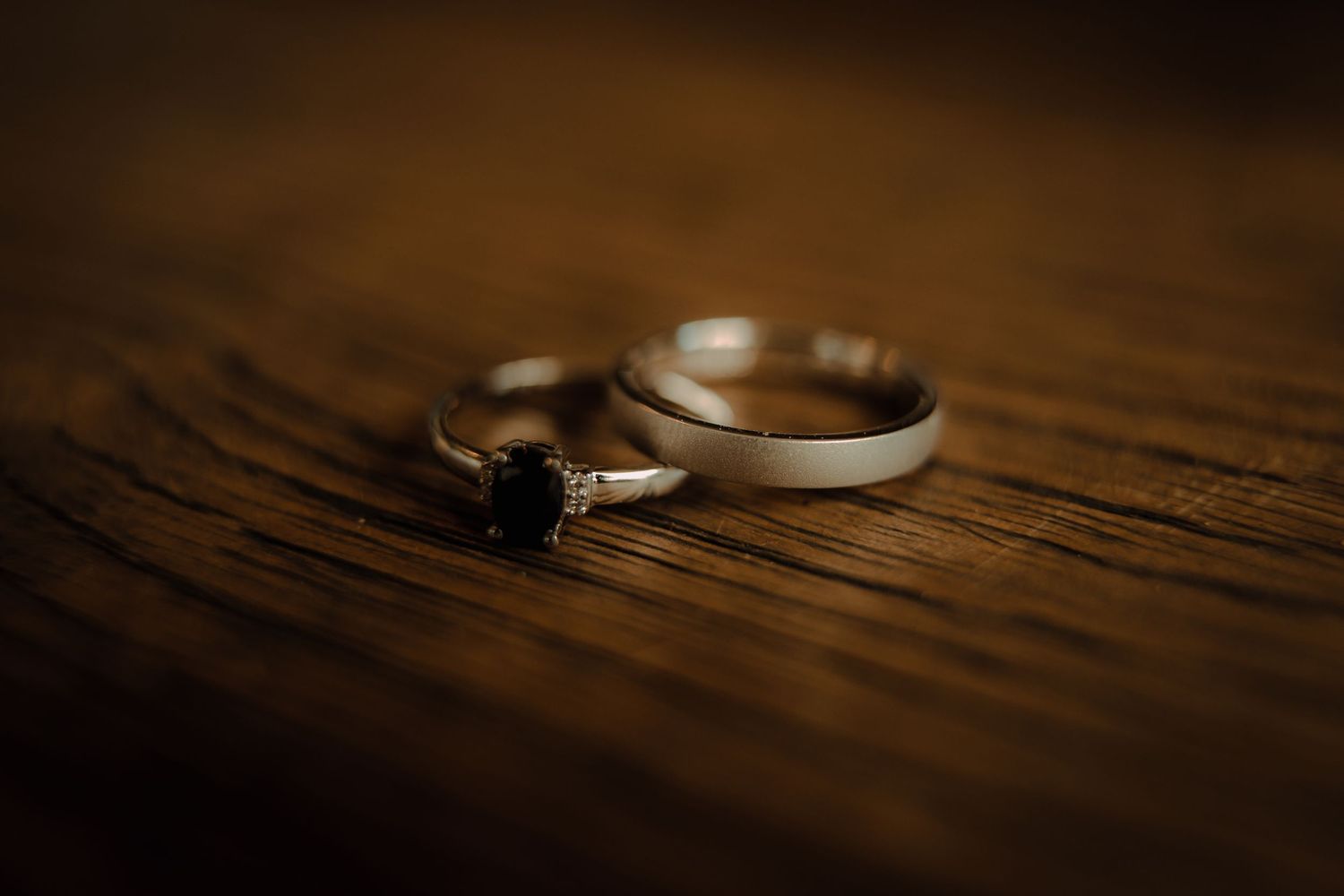 Wedding rings cast dramatic shadows on a rustic wooden surface in warm lighting.