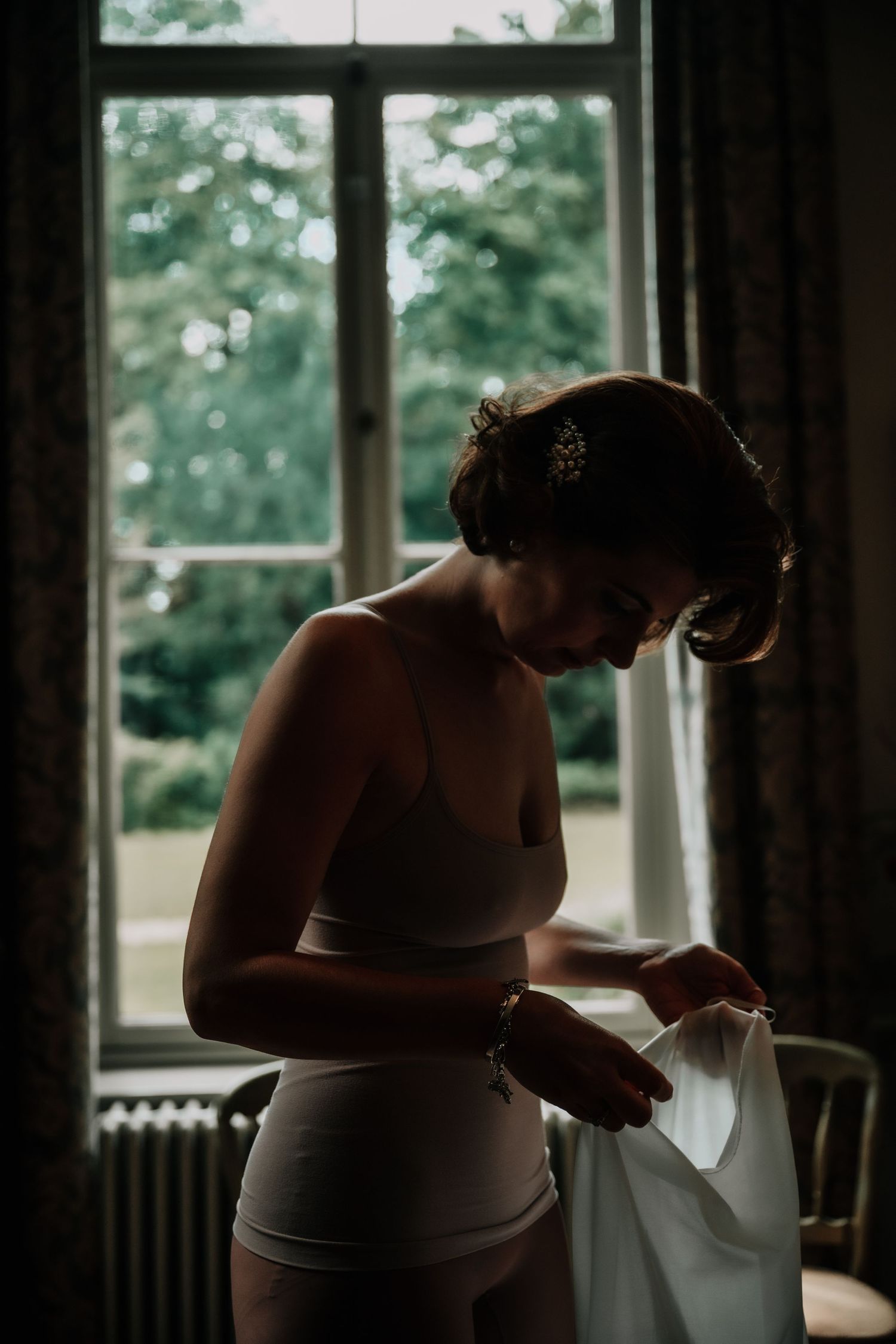 Silhouetted figure preparing in front of bright windows during wedding day preparations.
