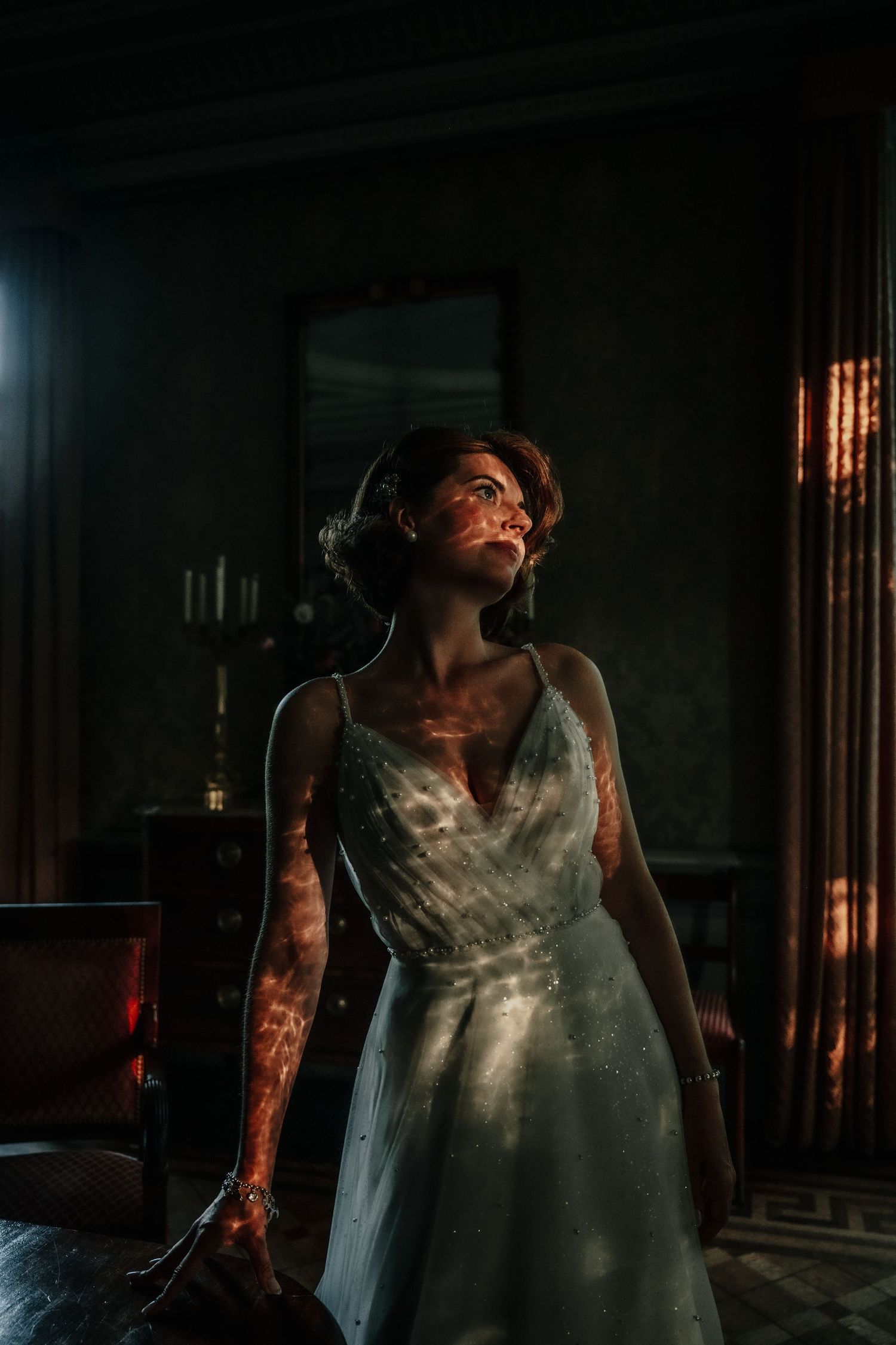 A dramatic silhouette in a white dress illuminated by warm window light.