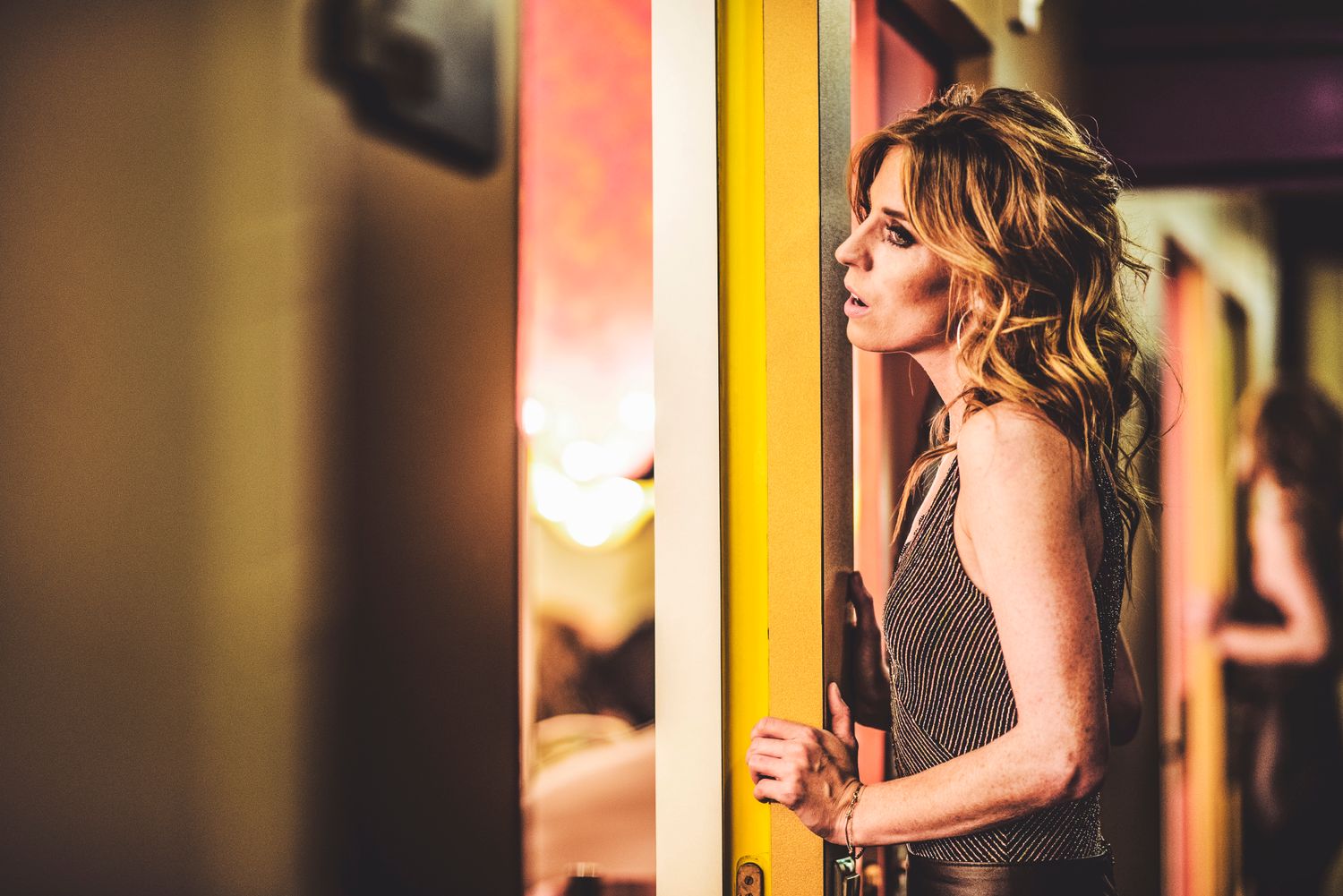 A person in a dark dress stands in a dimly lit room with yellow and warm lighting creating an atmospheric mood.