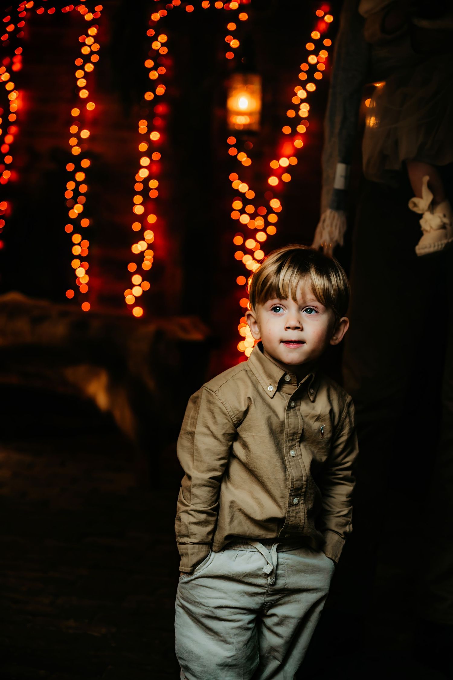 A child in a khaki button-down shirt and light pants poses playfully against a dark background with glowing orange lights.