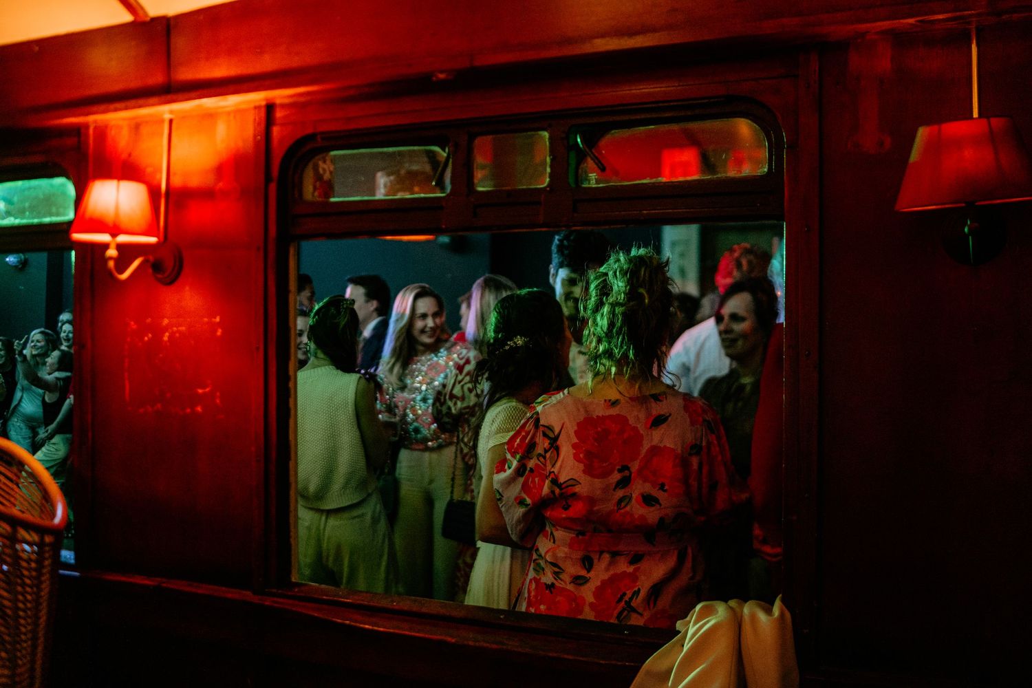 A red-lit bar interior features framed photographs on the wall creating an intimate atmosphere.