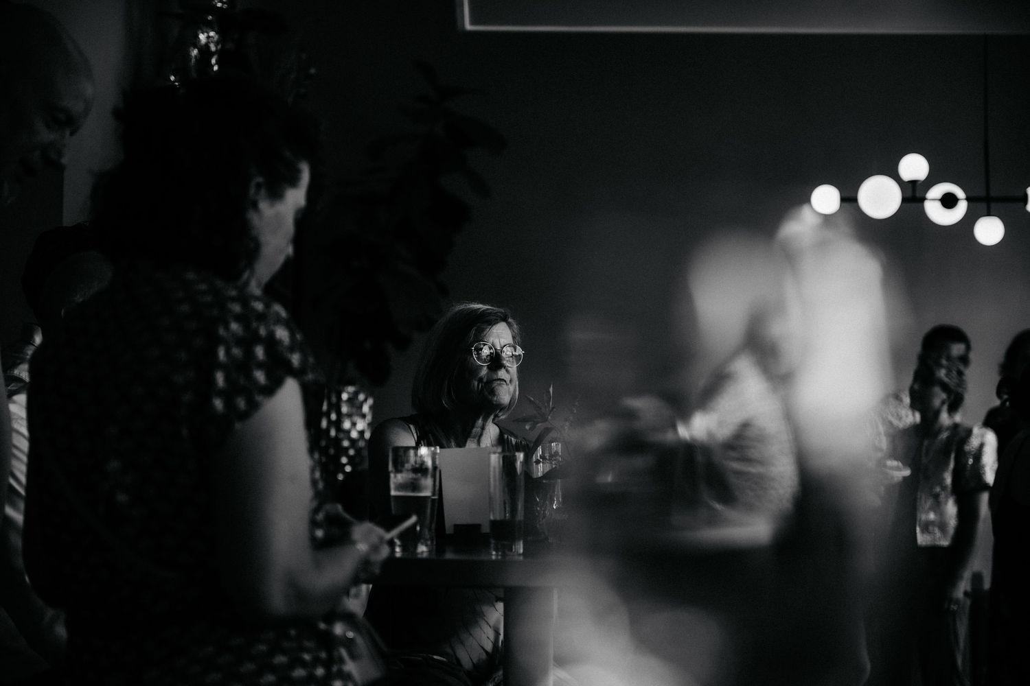 Blurred black and white photo of people dancing at a nighttime event with bokeh lights.